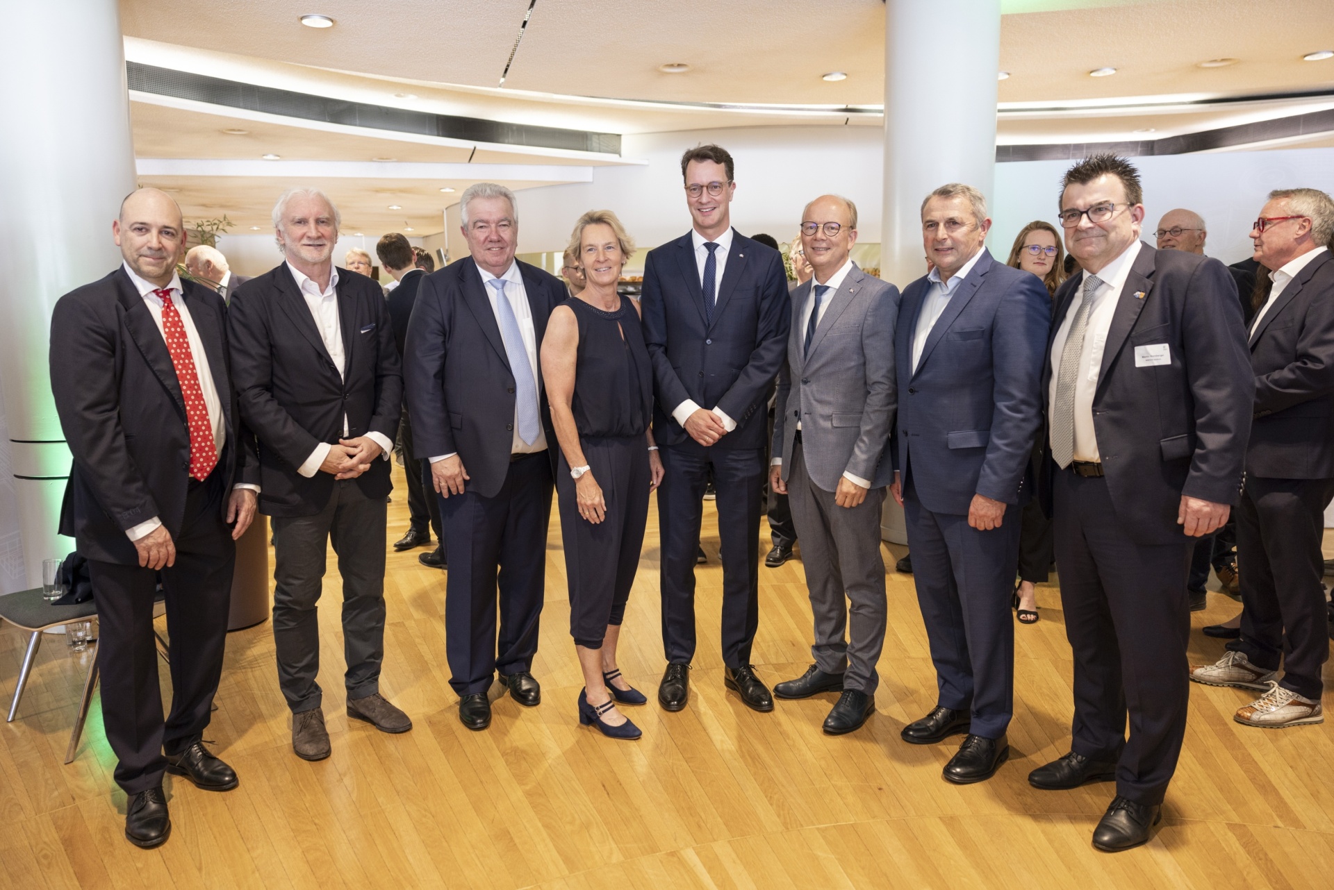 [{"clang_id":1,"value":"Gruppe von zehn berufskleideten Personen steht lächelnd in einem hellen Innenraum vor weißen Säulen."}]
