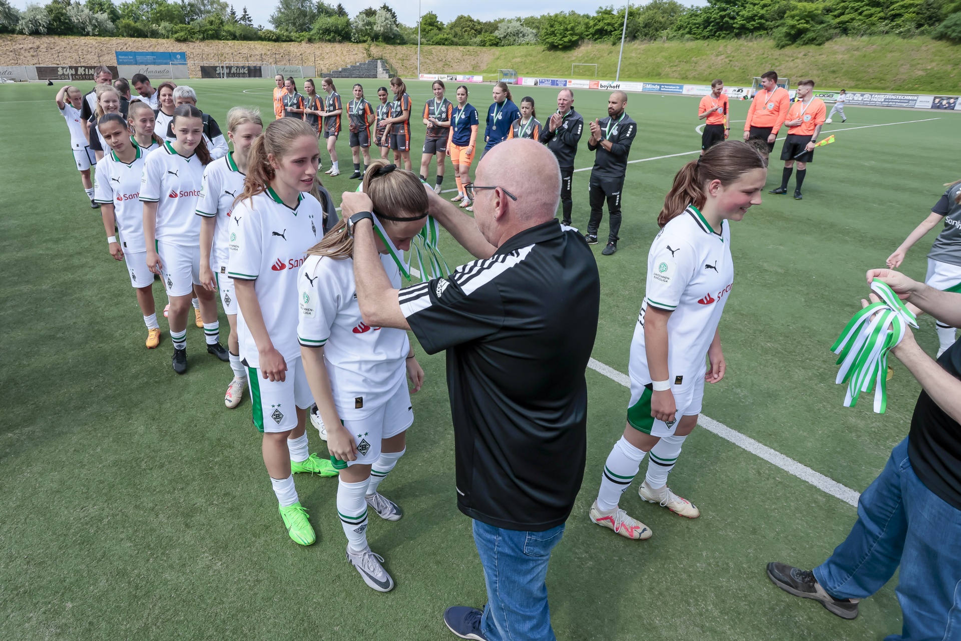 [{"clang_id":1,"value":"Fußballteam in grünen Trikots steht auf Spielfeld. Trainer spricht Spieler an. Im Hintergrund weitere Spieler und Zuschauer."}]