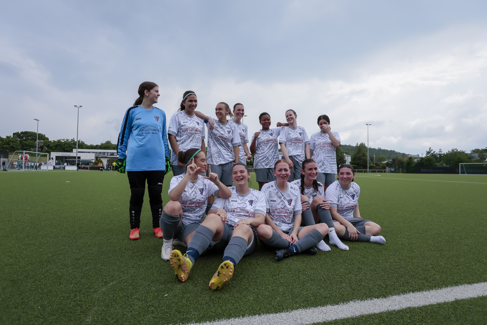 [{"clang_id":1,"value":"Fußballmannschaft, bestehend aus elf jungen Frauen, posiert auf einem grünen Kunstrasenplatz. Eine Spielerin steht, die anderen sitzen oder knien."}]