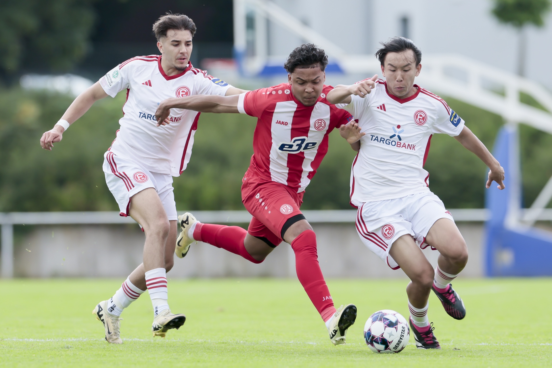 [{"clang_id":1,"value":"Drei Fußballspieler in rot-weißen Trikots auf grünem Rasen. Der Mittelspieler dribbelt den Ball, wird von den anderen flankiert."}]