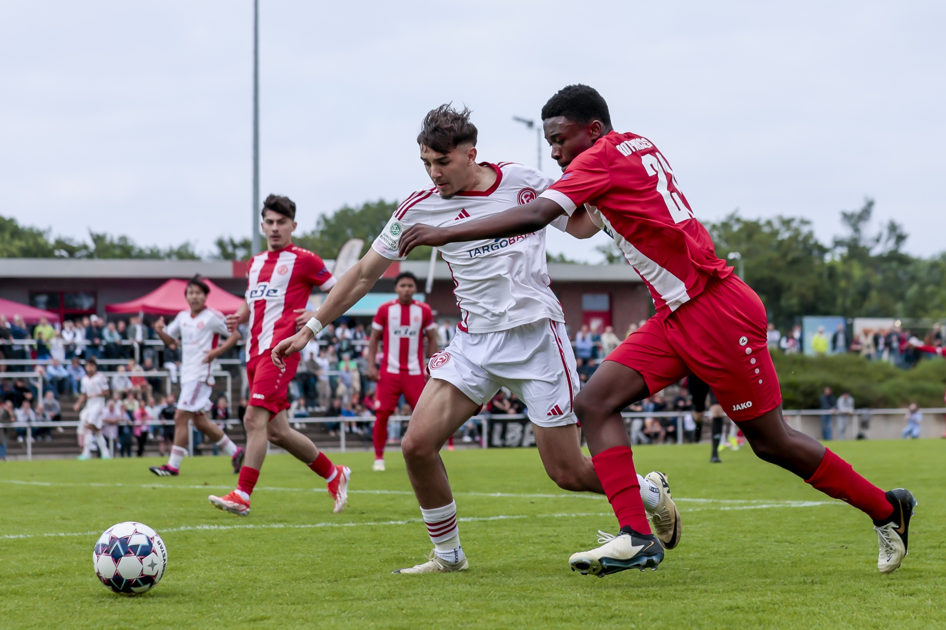 [{"clang_id":1,"value":"Fußballspiel: Zwei junge Spieler kämpfen um den Ball. Rot-weiße Trikots, grüner Rasen, Zuschauer im Hintergrund."}]