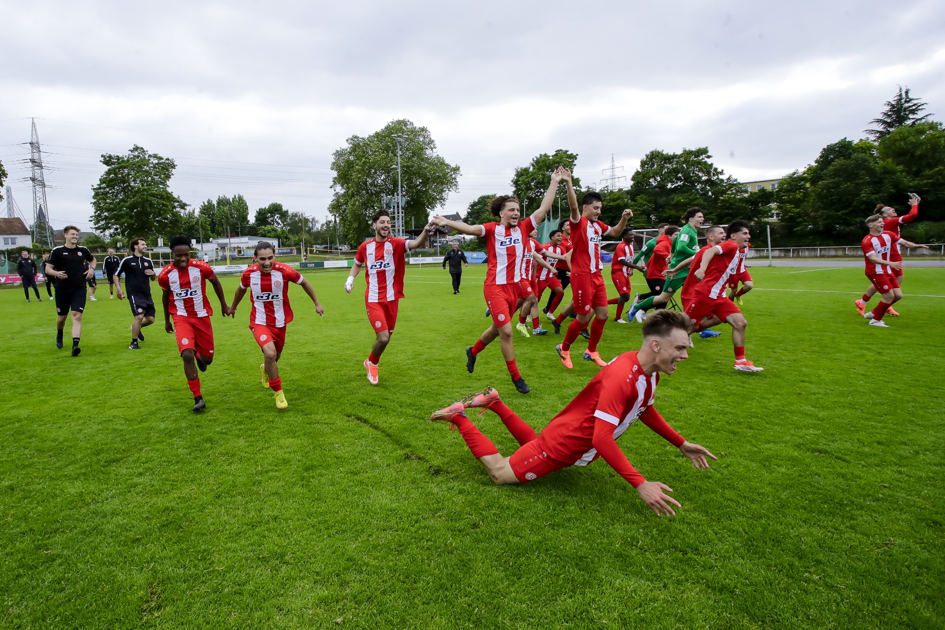 [{"clang_id":1,"value":"Fußballmannschaft in Rot-Weiß feiert auf grünem Rasen. Spieler jubeln, rennen und springen, einer liegt in der Bewegung vor Freude. Im Hintergrund Zuschauer und Bäume."}]
