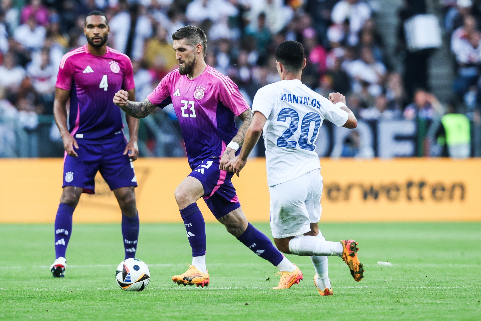[{"clang_id":1,"value":"Zwei Fußballspieler im Spiel. Links in Lila/Pink, rechts in Weiß, mit Ballkontakt. Im Hintergrund Zuschauerränge."}]