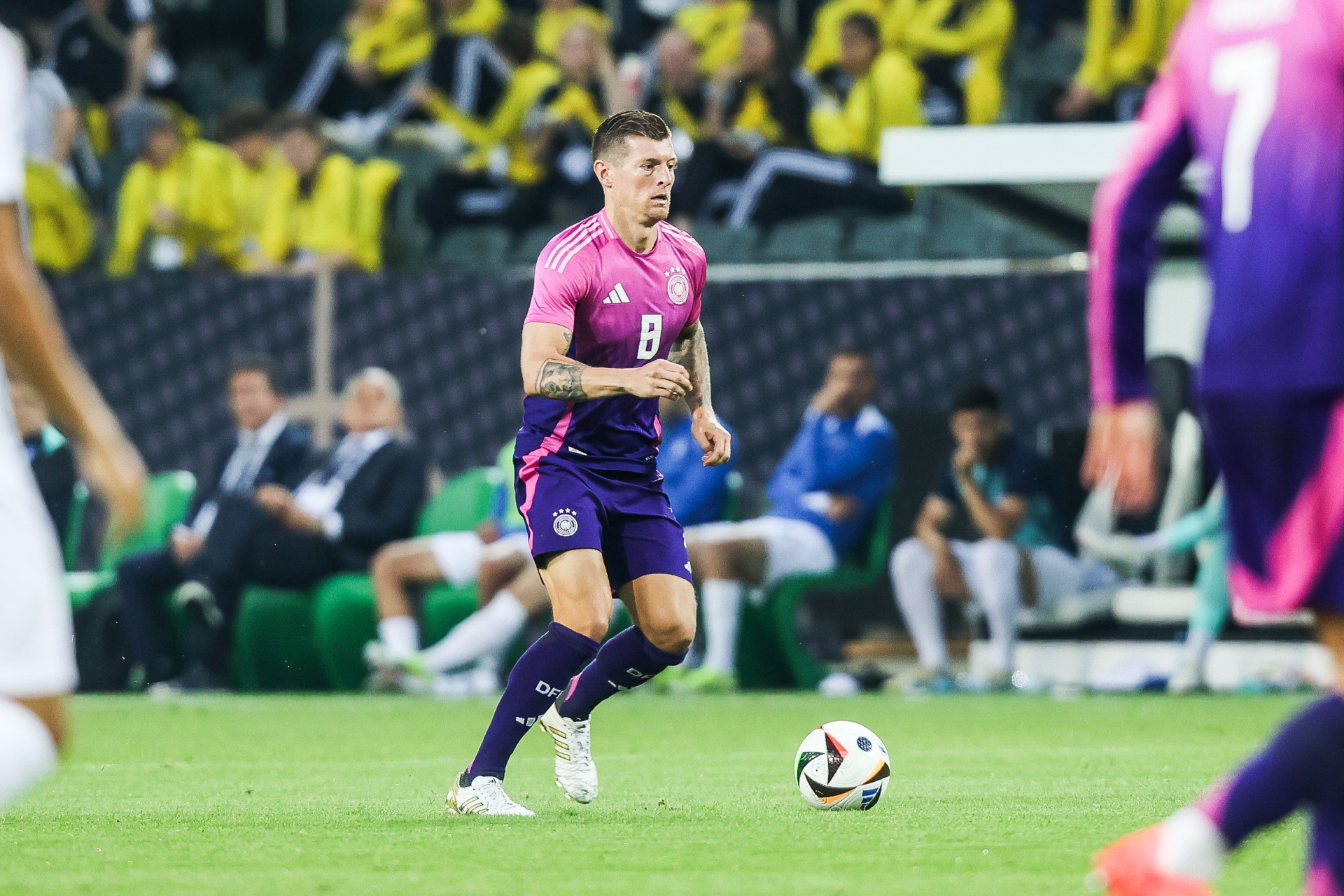 [{"clang_id":1,"value":"Fußballspieler mit Trikotnummer 8 und Shorts auf grünem Rasen, fokussiert auf Ball. Im Hintergrund Zuschauer und weitere Spieler."}]