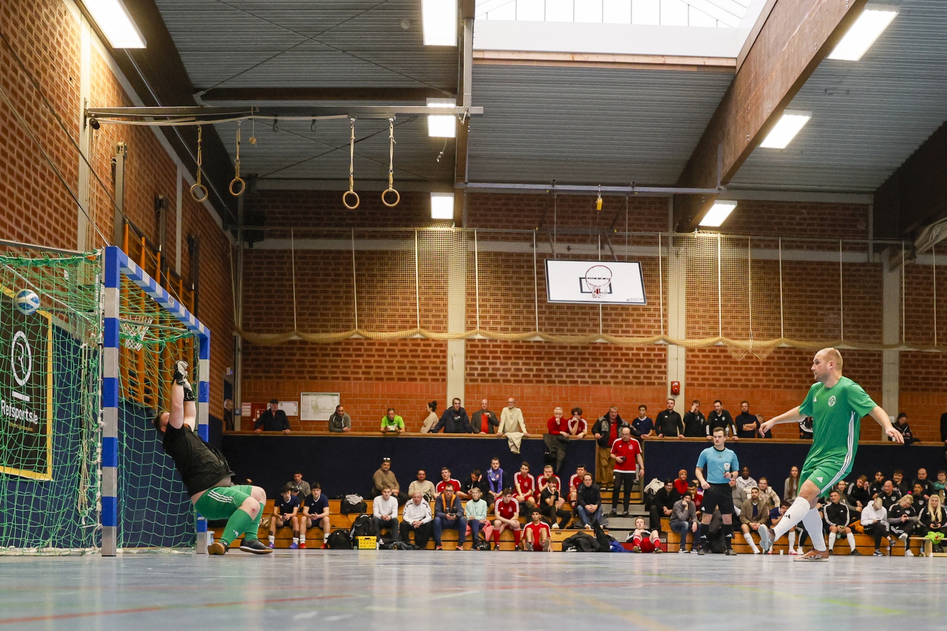 [{"clang_id":1,"value":"Handballspiel in Sporthalle. Spieler schießt, Torwart springt. Zuschauerreihen im Hintergrund."}]