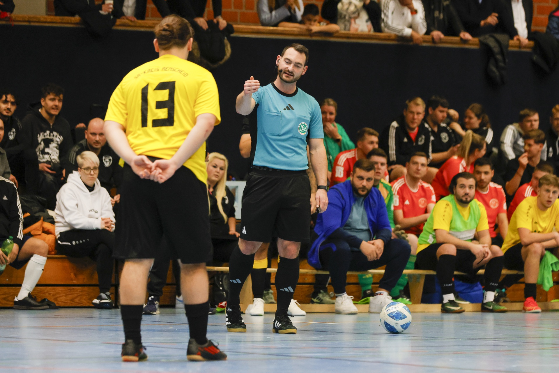 [{"clang_id":1,"value":"Handballspiel: Schiedsrichter mit erhobener Hand vor Spieler mit gelbem Trikot und Nummer 13. Zuschauer im Hintergrund."}]