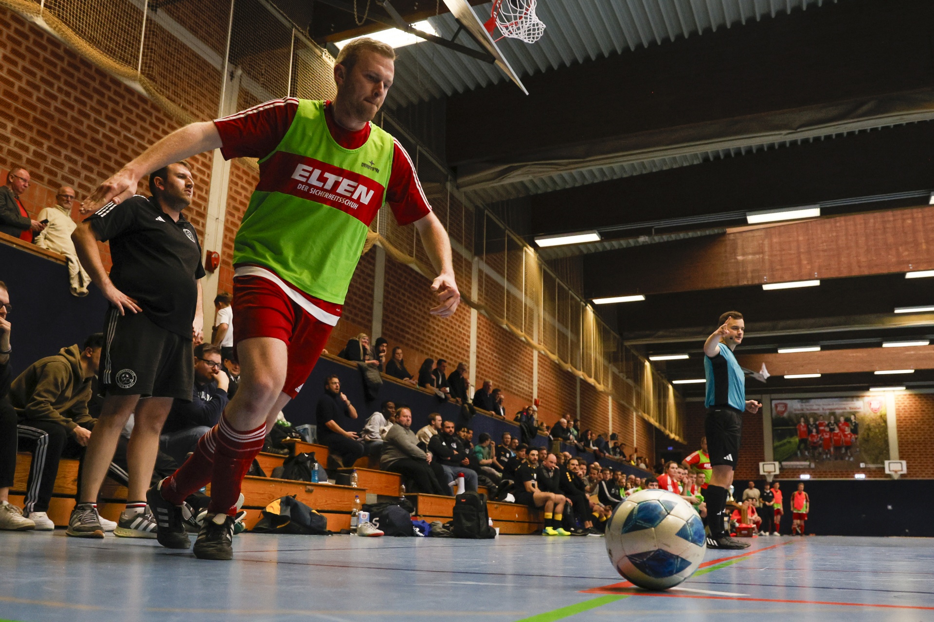 [{"clang_id":1,"value":"Handballspieler mit gelber Weste und roten Shorts dribbelt den Ball in einer Sporthalle vor Zuschauern. Im Hintergrund ein Schiedsrichter."}]