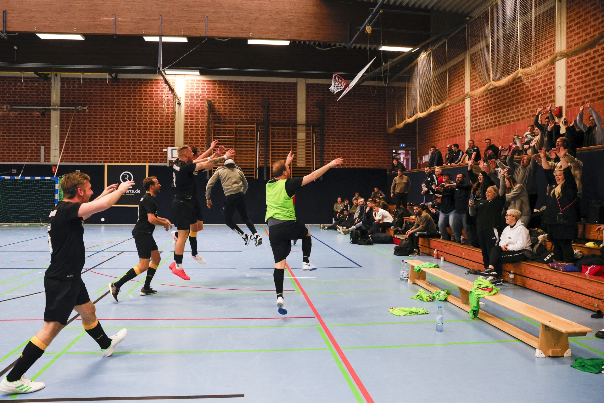 [{"clang_id":1,"value":"Floorball-Spiel in Sporthalle. Spieler mit Schlägern und Ball in Aktion. Zuschauerreihen rechts, dunkle Backsteinwand im Hintergrund."}]