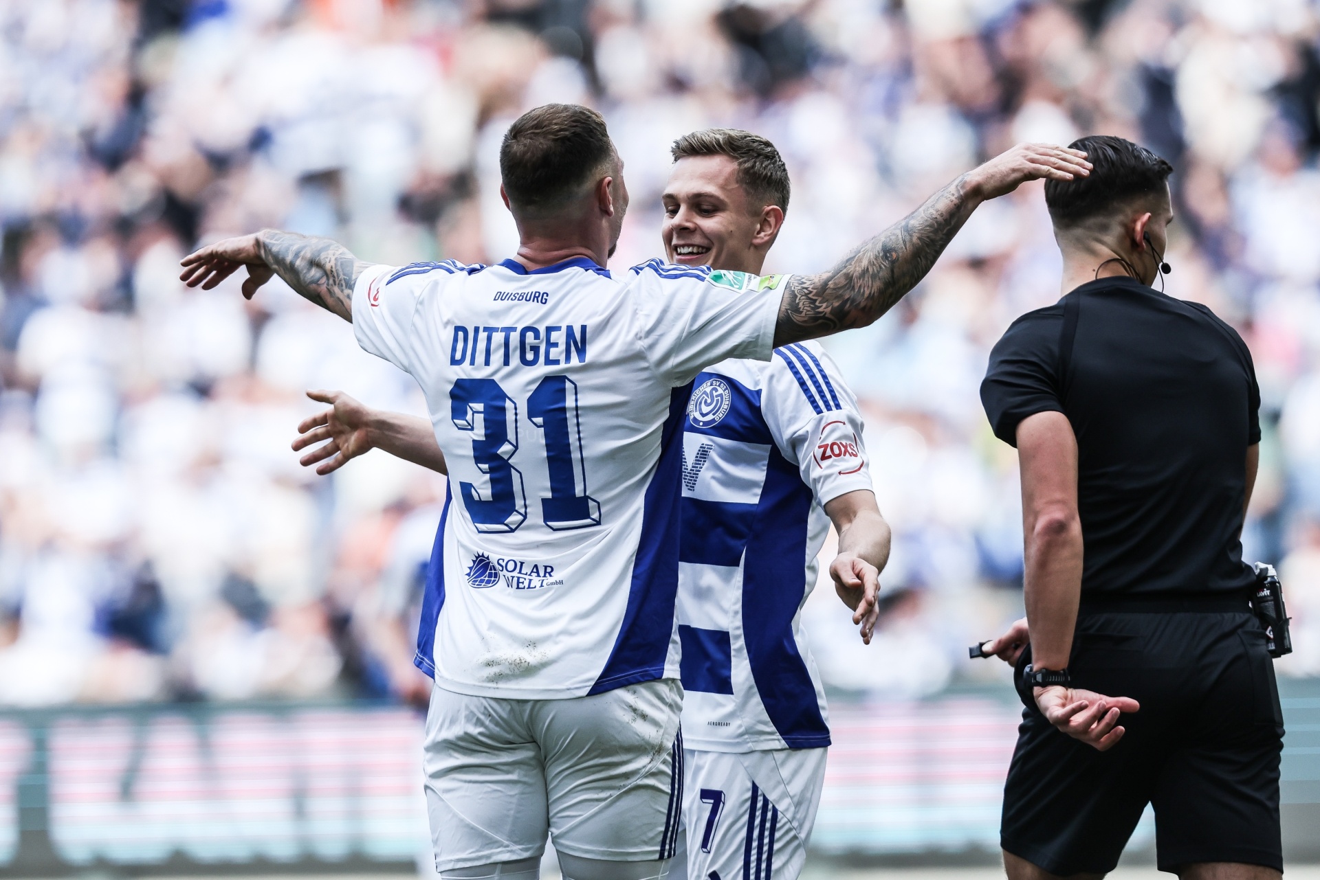 [{"clang_id":1,"value":"Zwei Fußballspieler von Duisburg mit den Nummern 31 und 7 feiern mit erhobenen Armen. Im Hintergrund ein Schiedsrichter und Zuschauer."}]