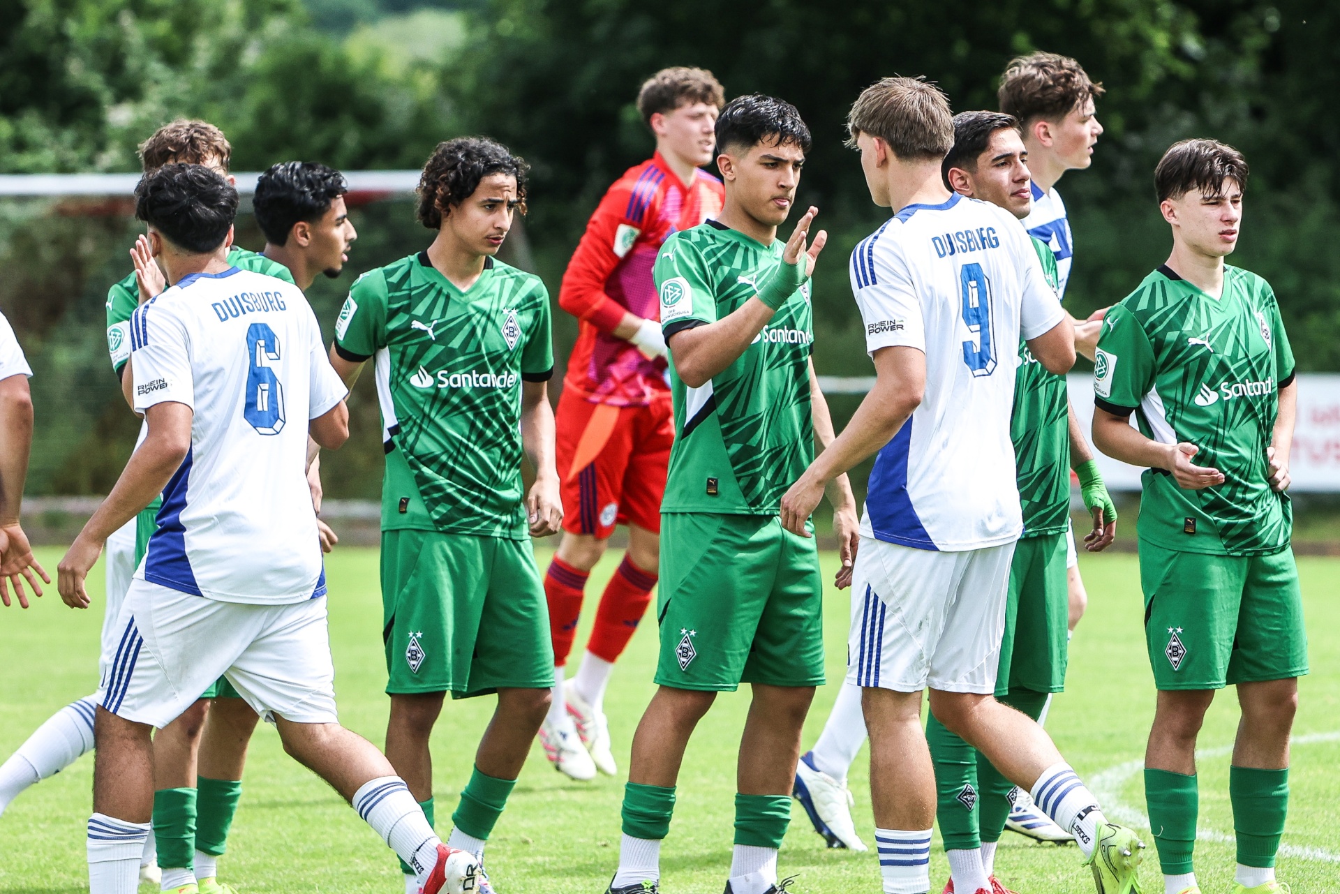 [{"clang_id":1,"value":"Fußballspieler in grünen und weißen Trikots stehen auf einem Rasenfeld. Einige Spieler diskutieren oder gestikulieren. Im Hintergrund sind weitere Spieler und ein rotes Trikot erkennbar."}]