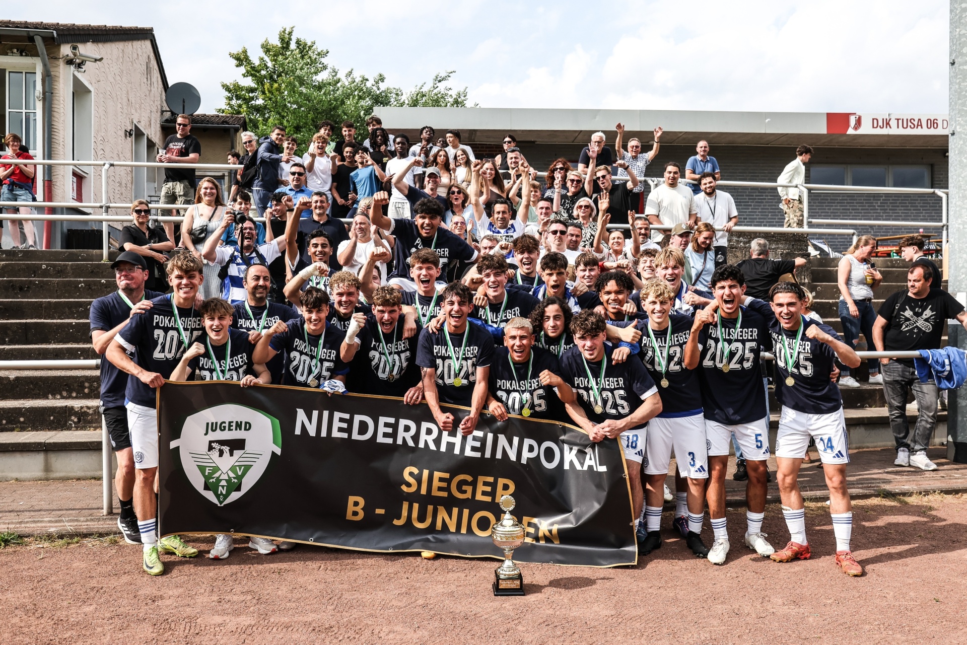 [{"clang_id":1,"value":"Fußballmannschaft mit Banner \"Niederrheinpokal Sieger B-Junioren\" und Pokal auf einer Tribüne vor Zuschauern."}]