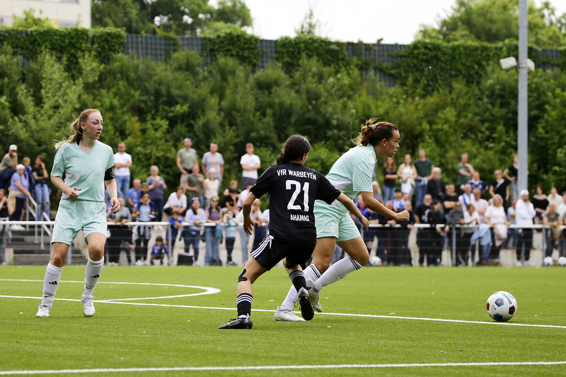 [{"clang_id":1,"value":"Zwei Fußballspielerinnen auf grünem Rasen verfolgen den Ball. Im Hintergrund Zuschauerreihen und Bäume."}]