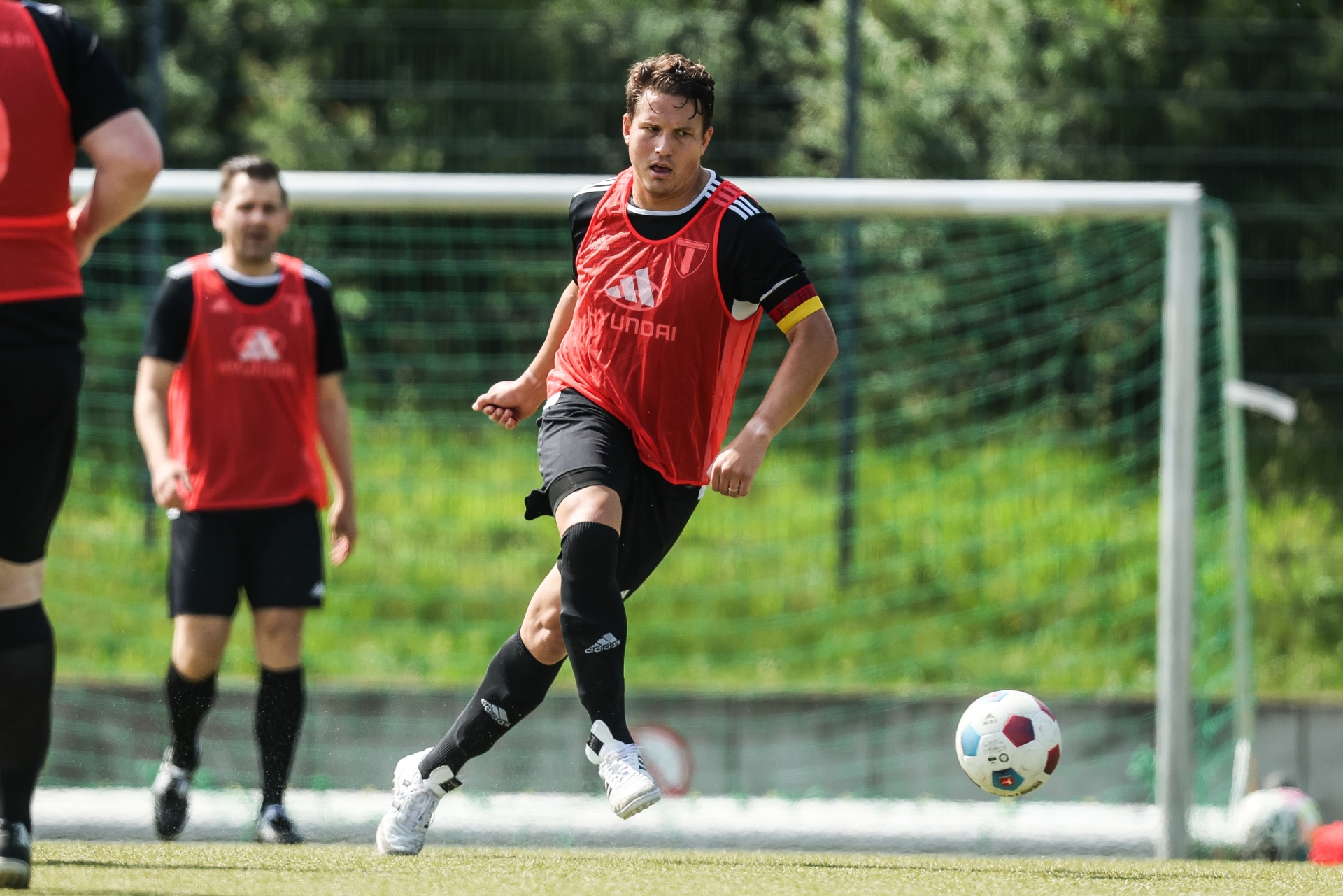 [{"clang_id":1,"value":"Fußballspieler in rotem Trikot schießt Ball auf grünem Rasen. Im Hintergrund weitere Spieler und ein Fußballtor."}]