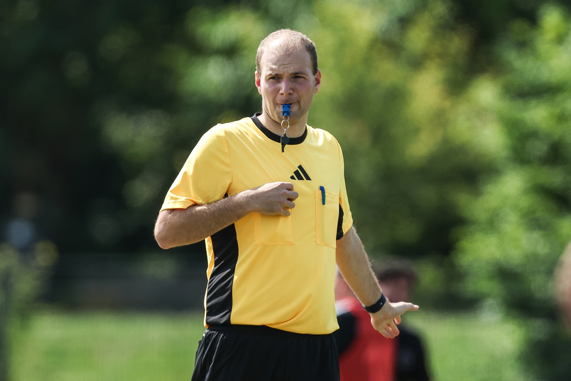 [{"clang_id":1,"value":"Schiedsrichter mit gelbem Trikot und schwarzer Hose pfeift mit der Pfeife und zeigt mit dem Finger auf etwas im Hintergrund."}]