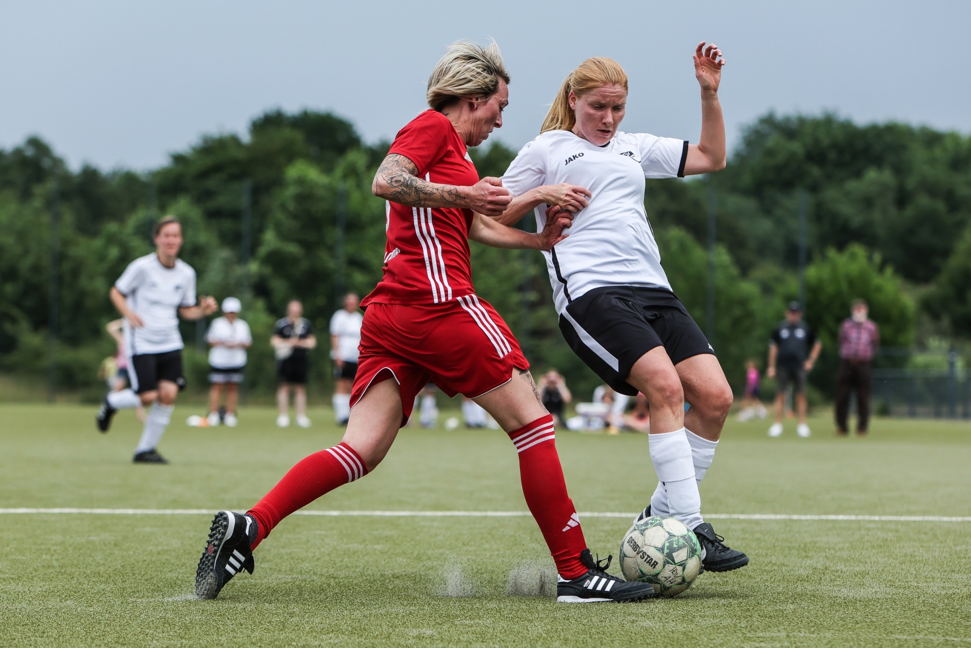 [{"clang_id":1,"value":"Zwei Fußballspielerinnen kämpfen um den Ball auf einem grünen Rasenplatz. Links rotes Trikot, rechts schwarz-weißes. Im Hintergrund weitere Spieler."}]
