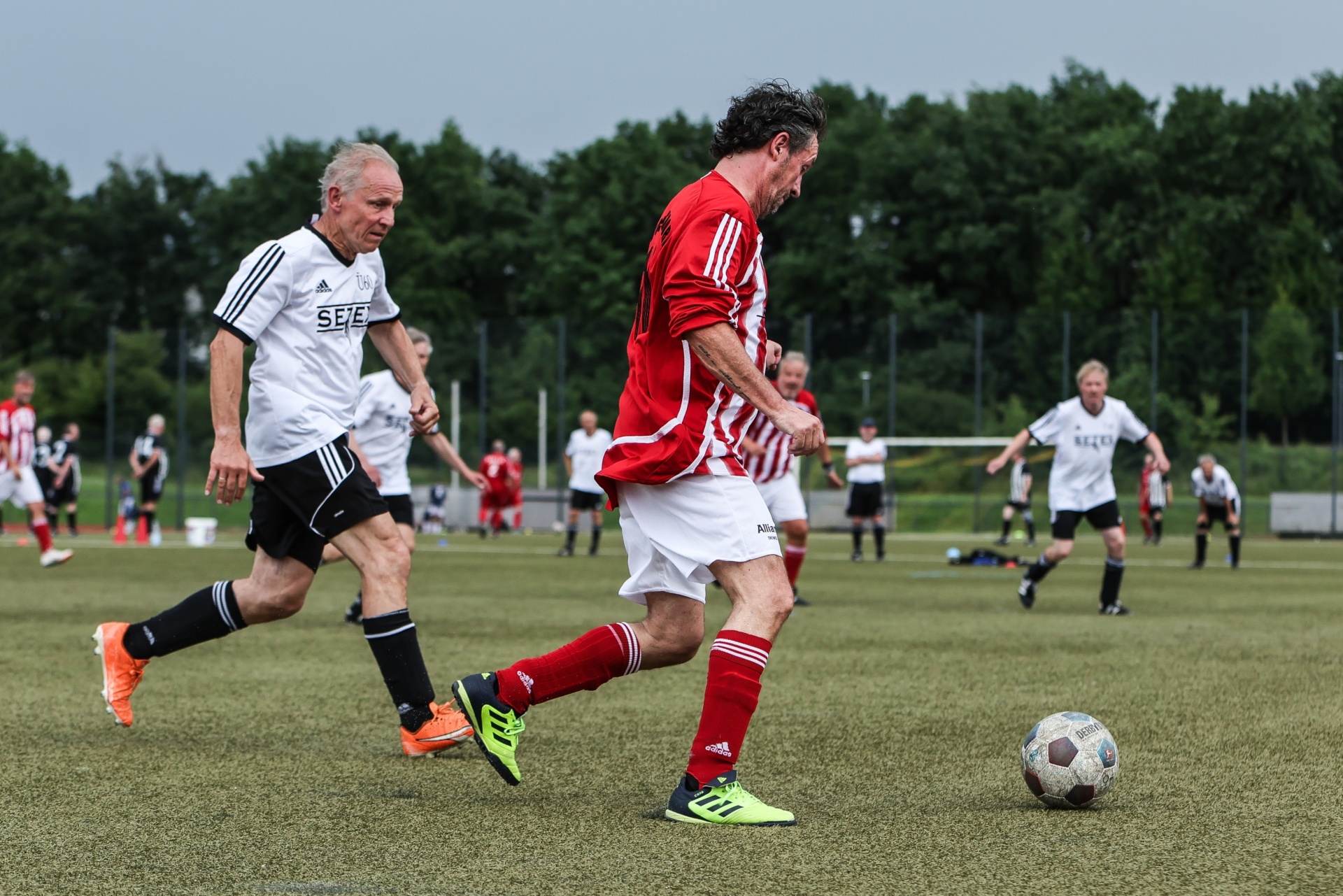 [{"clang_id":1,"value":"Zwei Fussballspieler auf grünem Kunstrasen. Links ein älterer Mann in weissem Trikot, rechts ein Mann in rotem Trikot, der den Ball schiesst."}]