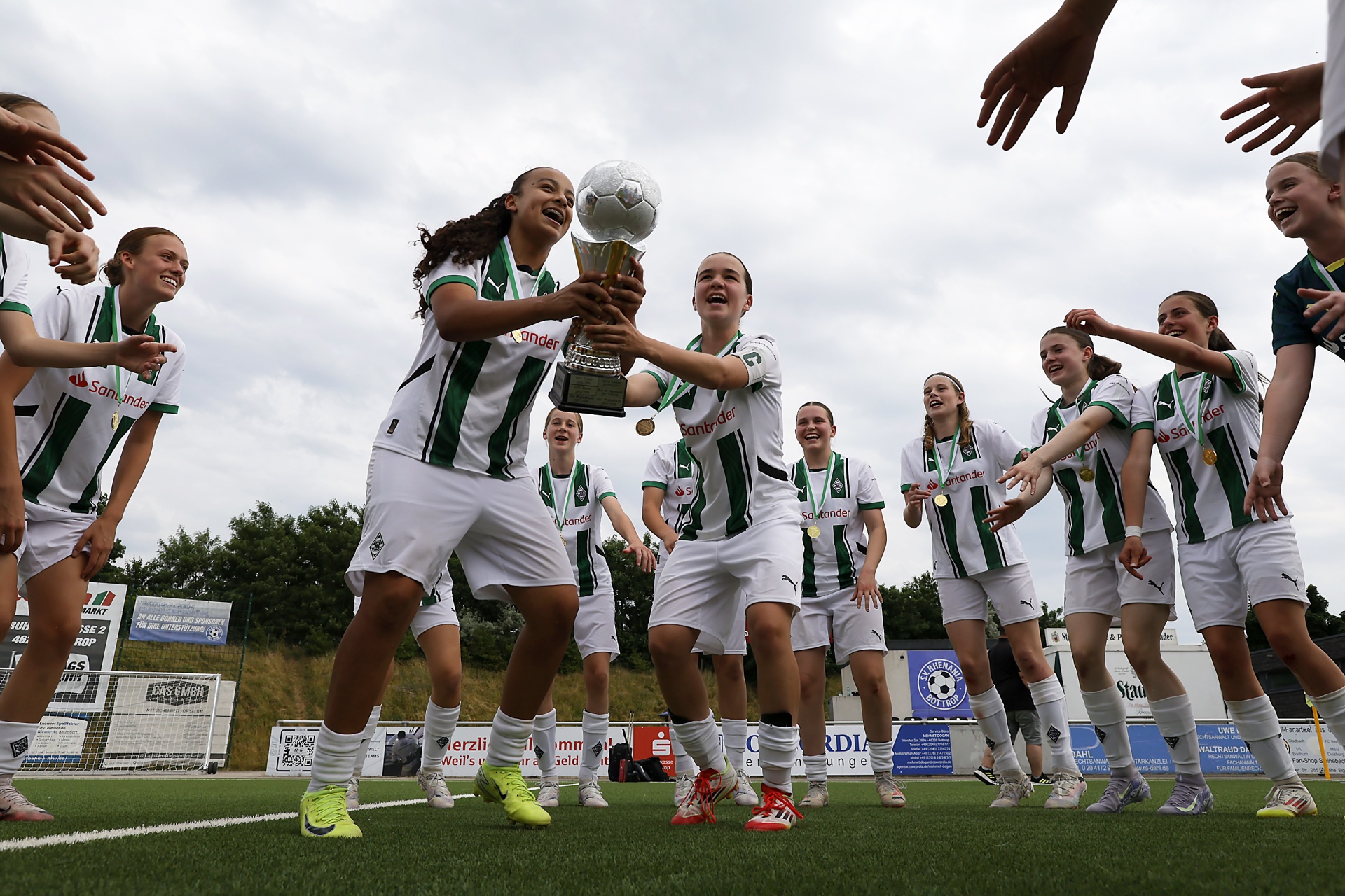[{"clang_id":1,"value":"Frauenfußballteam jubelt auf einem Rasenplatz. Eine Spielerin hält eine Trophäe hoch, die anderen feiern mit erhobenen Armen. Grünes und weißes Trikot."}]