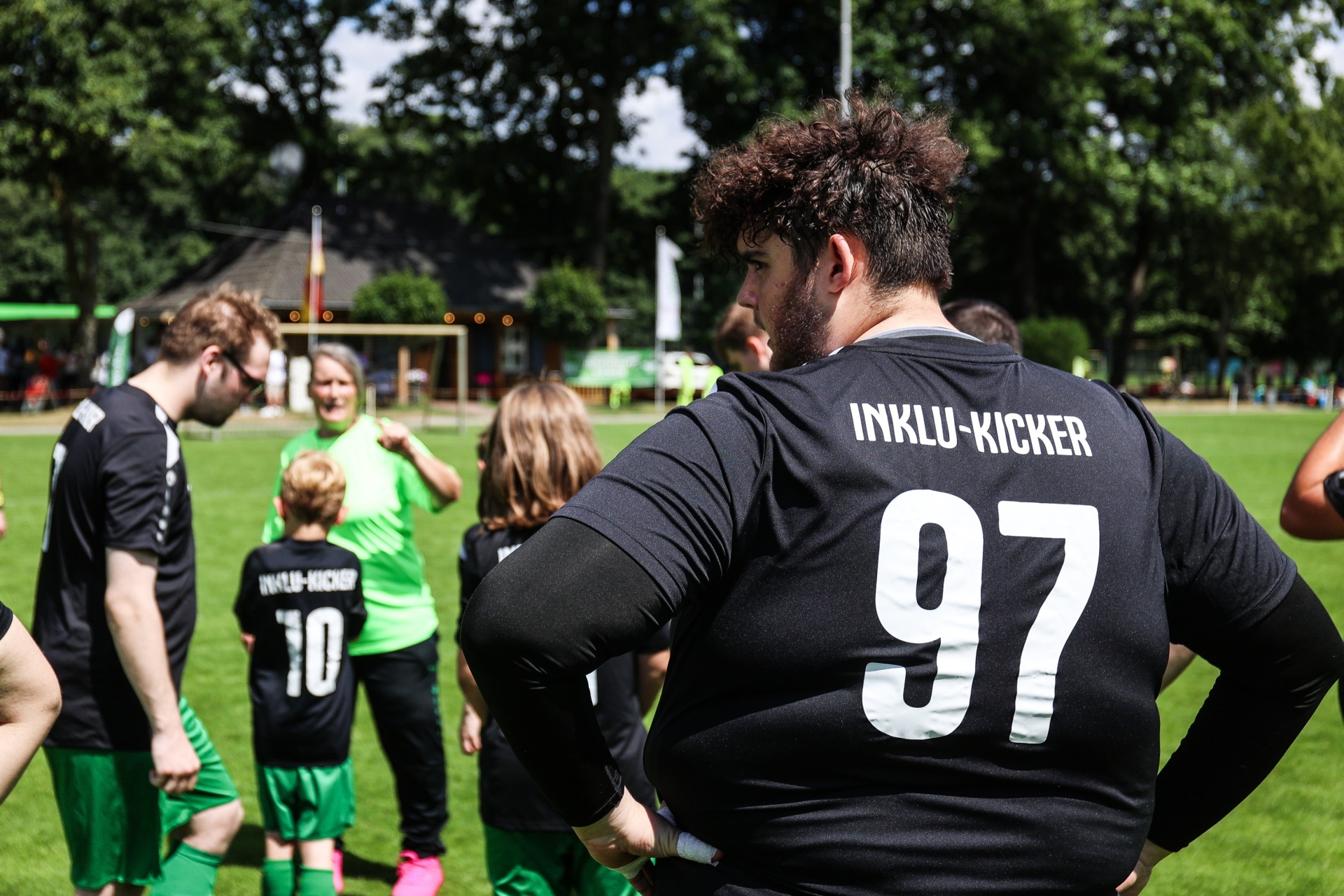 [{"clang_id":1,"value":"Fußballteam im Kreis. Vordergrund: Spieler mit schwarzem Trikot, Nummer 97, Rückenansicht. Hintergrund: weitere Spieler und Fußballfeld."}]