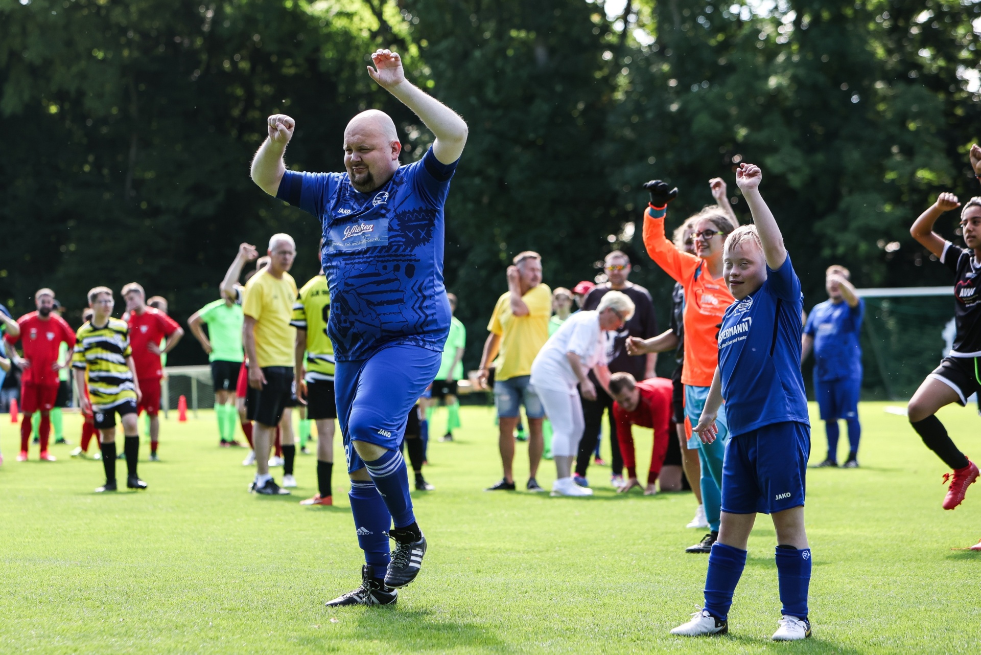 [{"clang_id":1,"value":"Zwei Fußballspieler in blauen Trikots jubeln auf einem grünen Rasenfeld. Im Hintergrund weitere Spieler und Zuschauer."}]