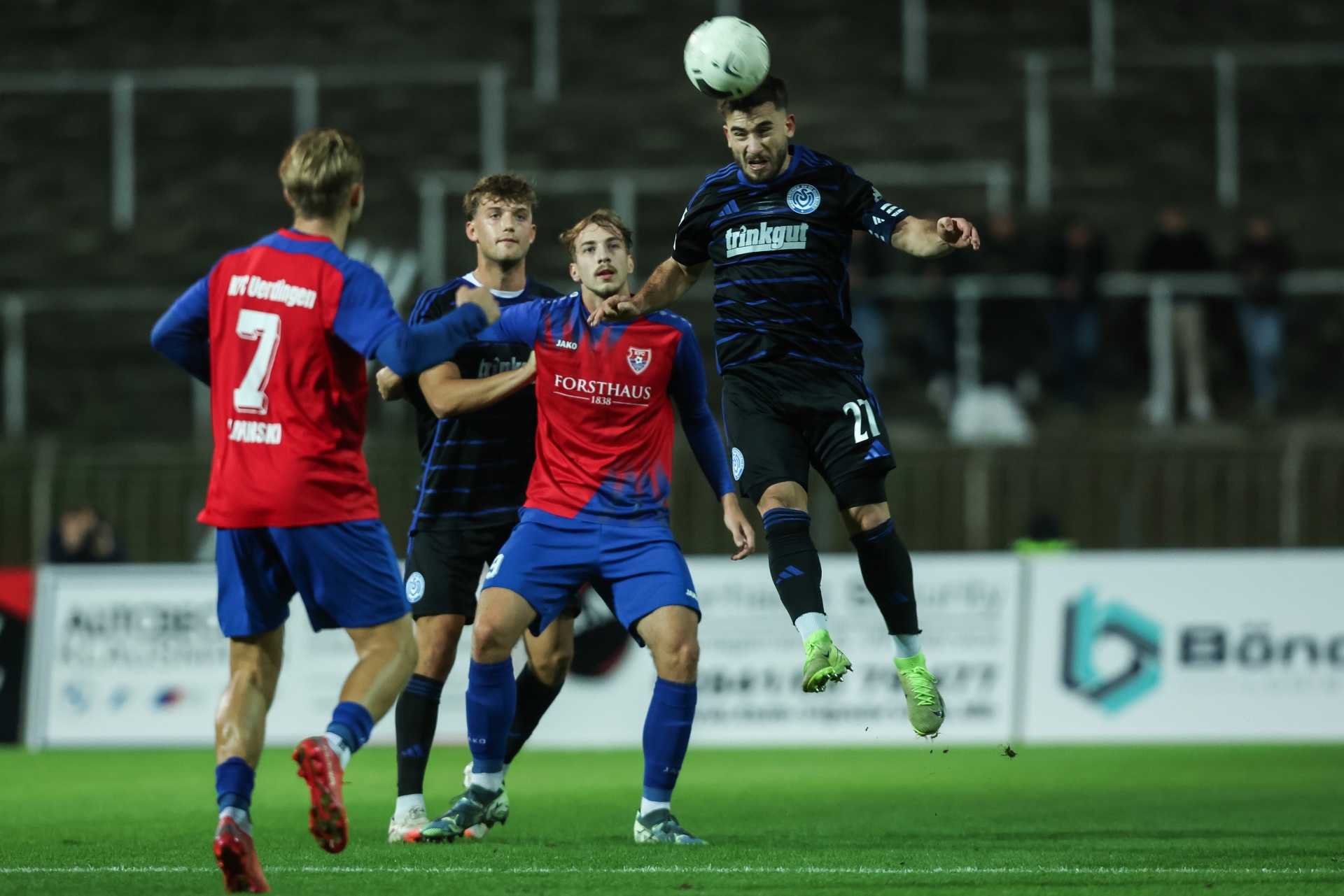 [{"clang_id":1,"value":"Fußballspiel: Spieler springt hoch, um Kopfball zu spielen. Weitere Spieler in blau-roten Trikots im Hintergrund auf dem Rasen. Stadion im Dunkeln."}]
