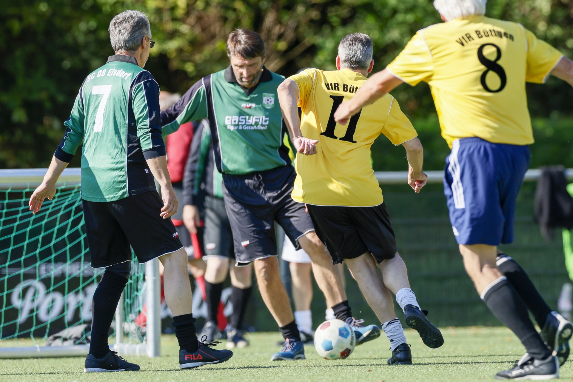 [{"clang_id":1,"value":"Fußballspiel: Vier Spieler auf grünem Kunstrasen, darunter ein Torwart. Spieler tragen Trikots mit Nummern und Vereinsnamen. Ball im Spiel."}]