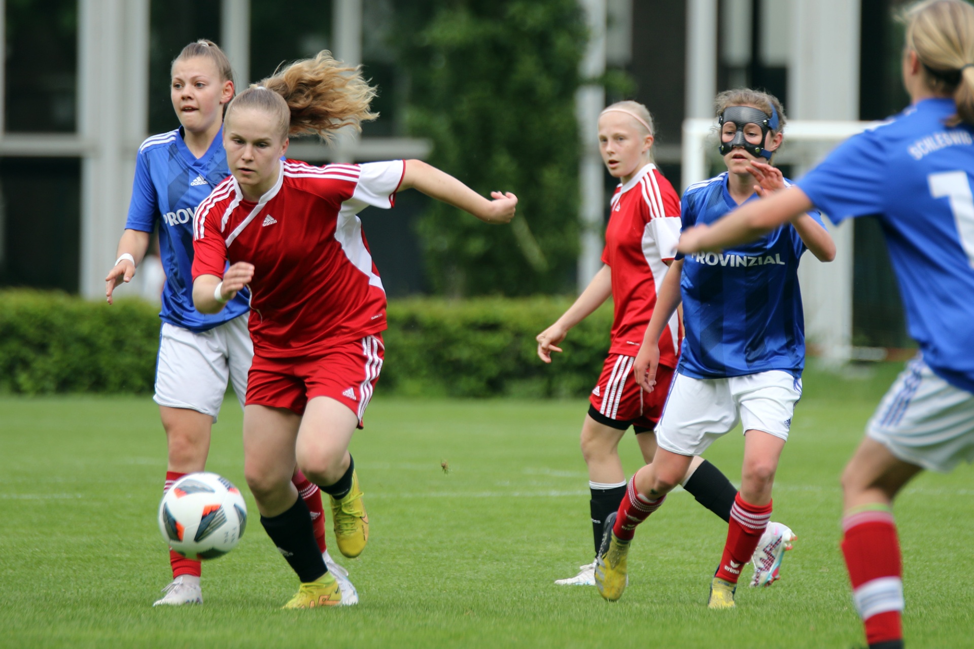 [{"clang_id":1,"value":"Fußballspiel mit vier jungen Spielerinnen auf grünem Rasen. Eine Spielerin dribbelt den Ball, die anderen verfolgen sie. Blaue und rote Trikots."}]