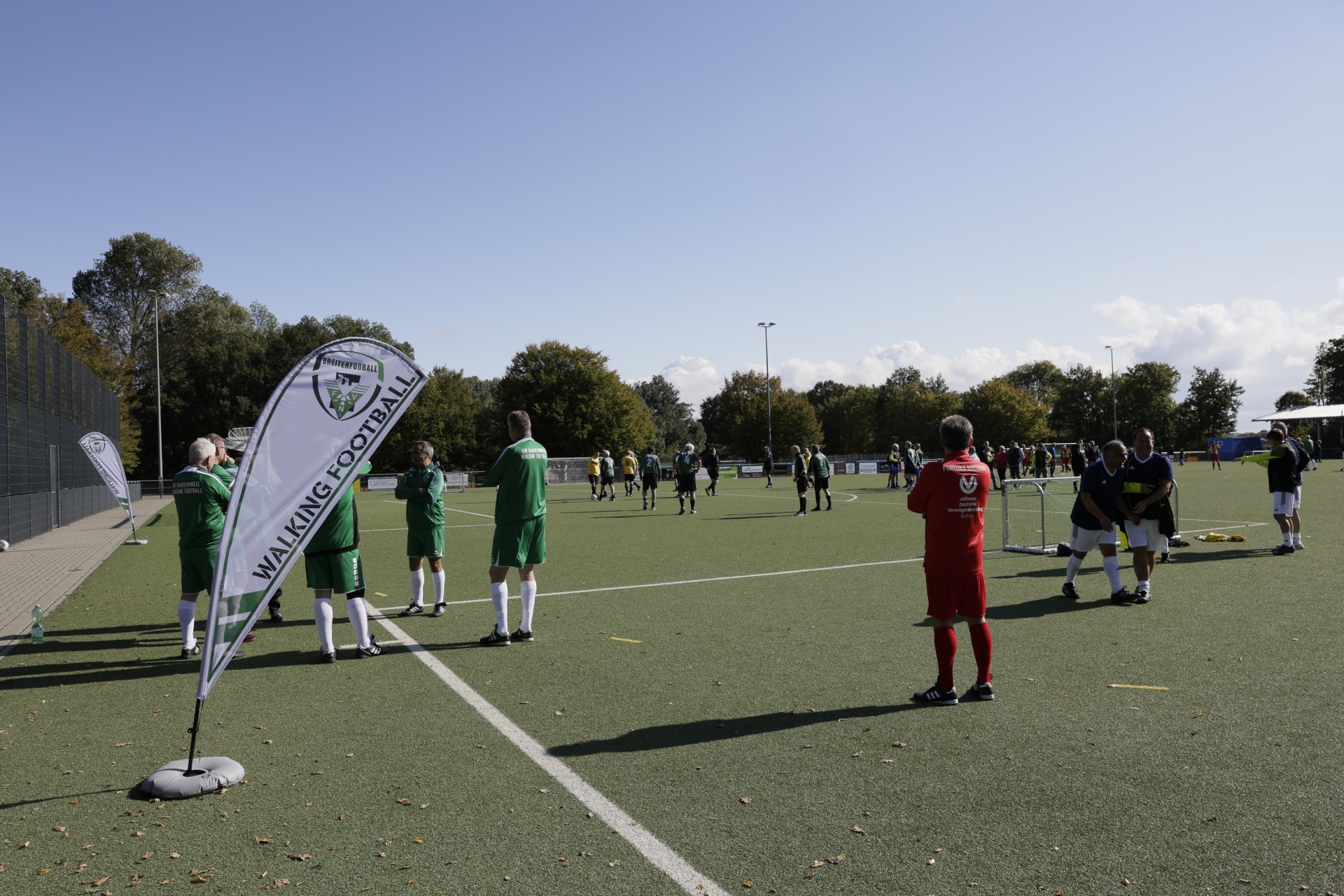 [{"clang_id":1,"value":"Fußballfeld mit spielenden Menschen. Links ein Banner mit der Aufschrift \"Walking Football\". Im Hintergrund Bäume und ein blauer Himmel."}]