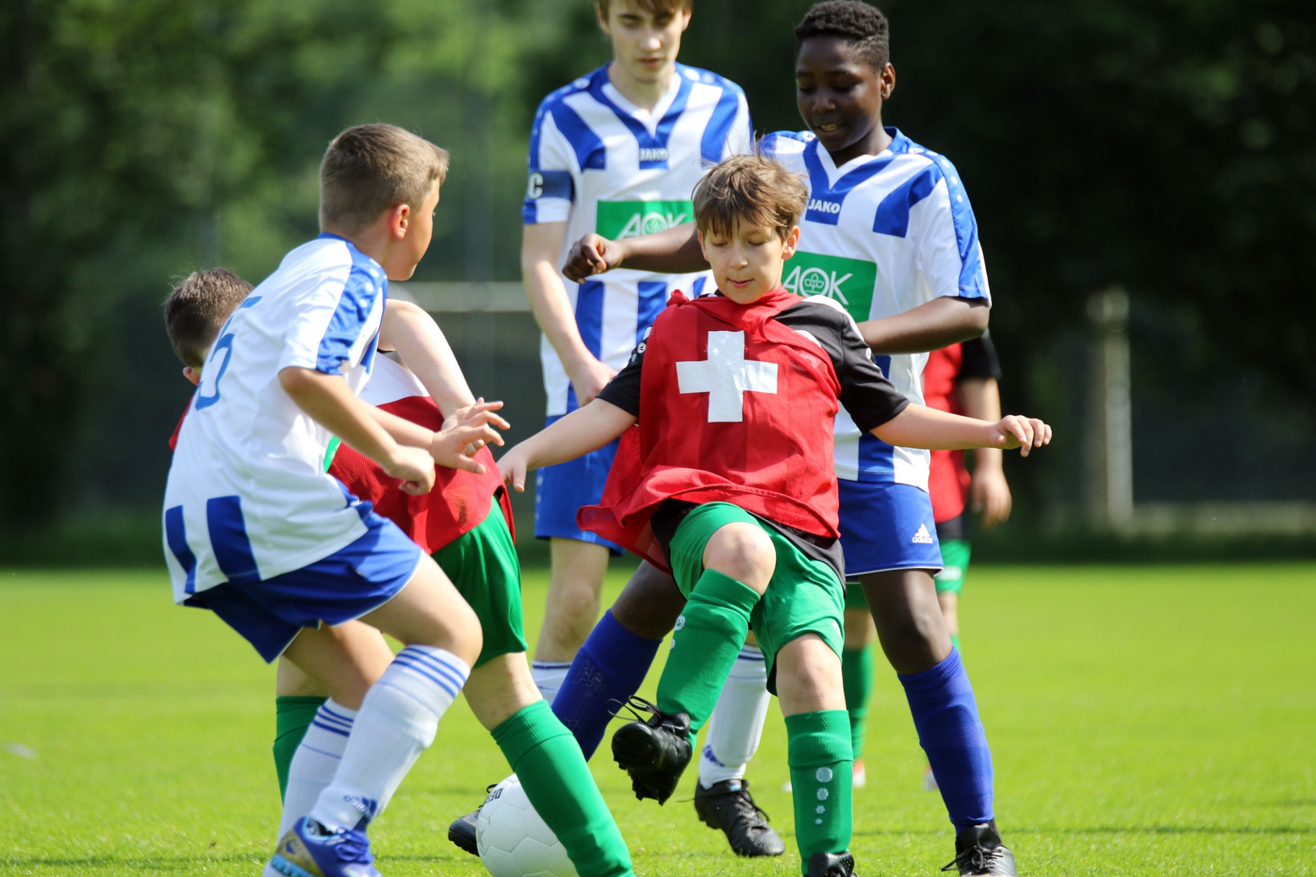 [{"clang_id":1,"value":"Fußballspiel mit vier Jungen auf Grün. Ein Spieler in Rot versucht, den Ball zu kicken, während ihn zwei Gegenspieler in Blau und Weiß bedrängen. Im Hintergrund weitere Spieler."}]