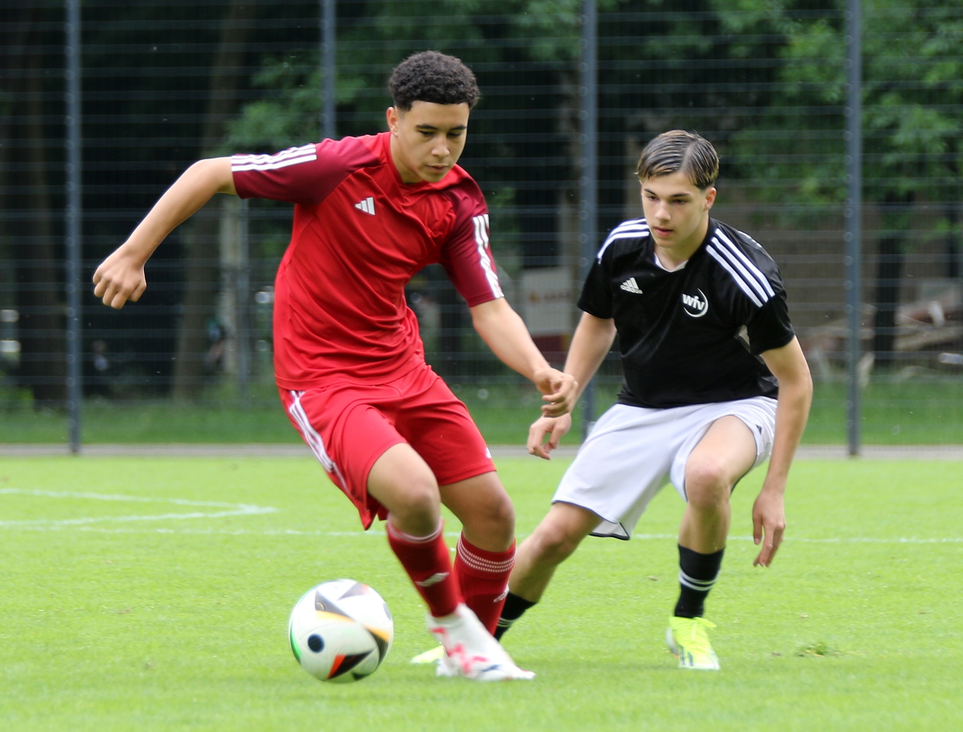 [{"clang_id":1,"value":"Zwei Fussballspieler auf grünem Rasen. Links ein Spieler in rotem Trikot mit Ball, rechts ein Spieler in schwarz-weiss. Beide in Aktion."}]