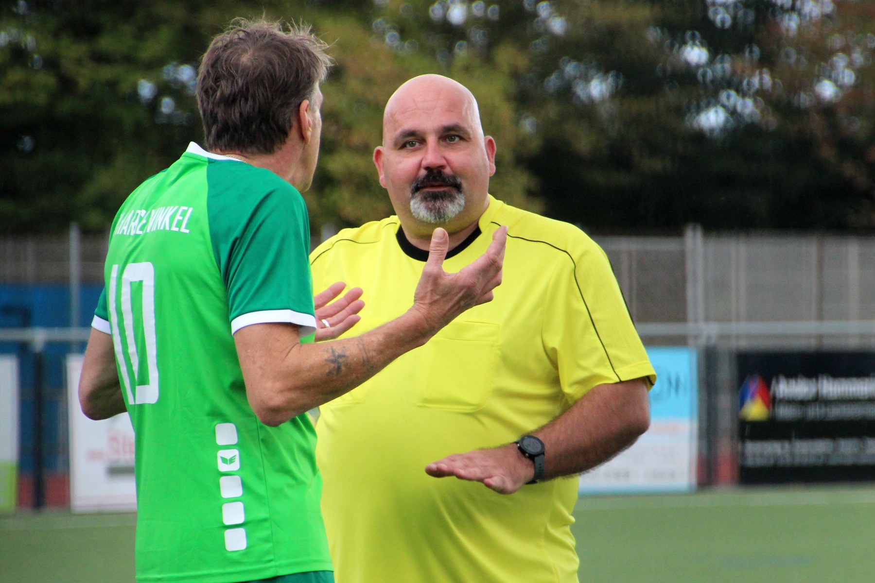 [{"clang_id":1,"value":"Zwei Männer diskutieren auf einem Fußballfeld. Links ein Spieler mit grünem Trikot, rechts ein Schiedsrichter in gelber Kleidung."}]