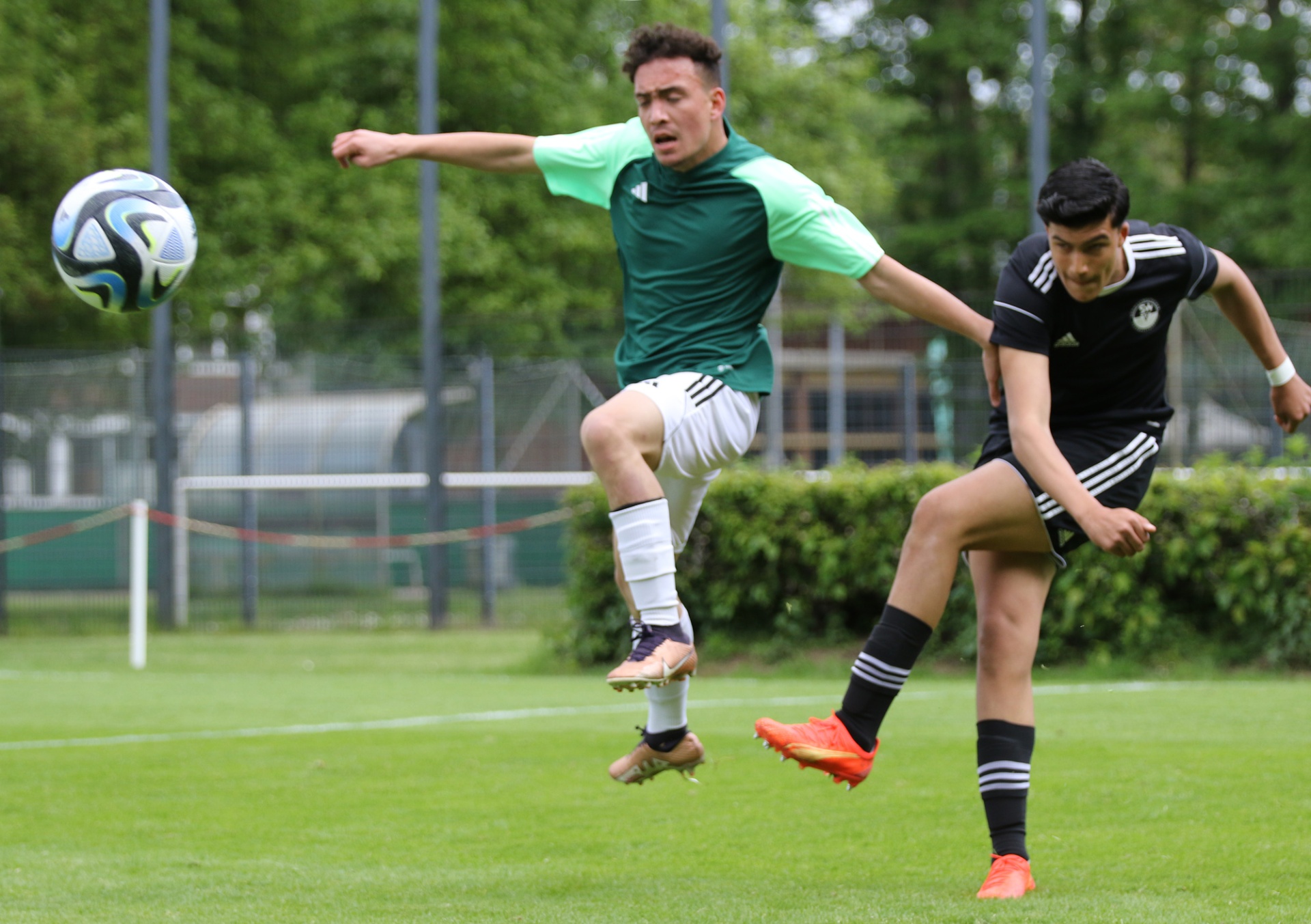 [{"clang_id":1,"value":"Zwei Fußballspieler kämpfen um einen Ball. Ein Spieler in grün-weißem Trikot versucht, den Ball per Kopf zu spielen, während ein Spieler in schwarz-weißem Trikot ihm entgegenkommt. Hintergrund: Grünfläche und Zaun."}]
