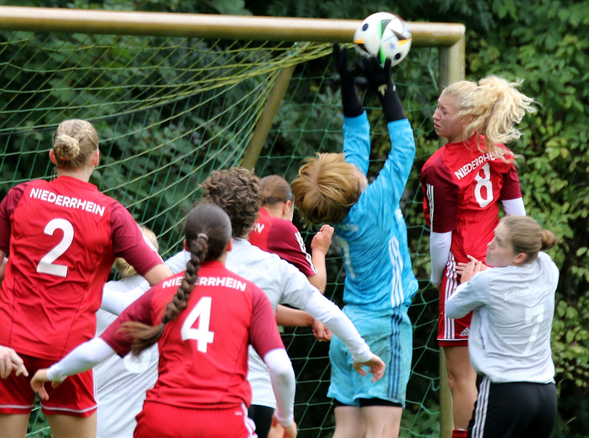[{"clang_id":1,"value":"Fußballspiel: Frauen kämpfen um Ball vor Tor. Rote, blau-weiße und weiße Trikots. Netzen im Hintergrund."}]