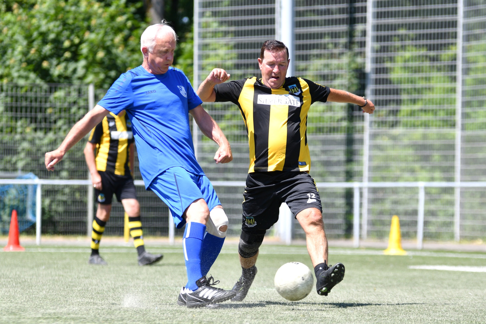 [{"clang_id":1,"value":"Zwei Fußballspieler im Spiel. Links ein Spieler in blauem Trikot, rechts in schwarz-gelbem Trikot mit der Nummer 12. Sie kämpfen um den Ball auf einem Rasenplatz."}]