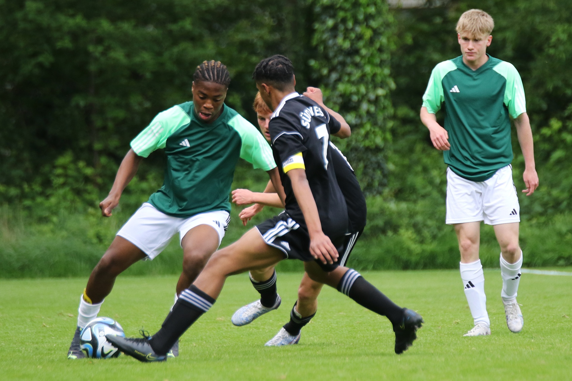 [{"clang_id":1,"value":"Fußballspiel: Vier junge Spieler auf grünem Rasen. Zwei tragen grüne, zwei schwarz-weiße Trikots. Ein Spieler schießt auf das Tor. Bäume im Hintergrund."}]