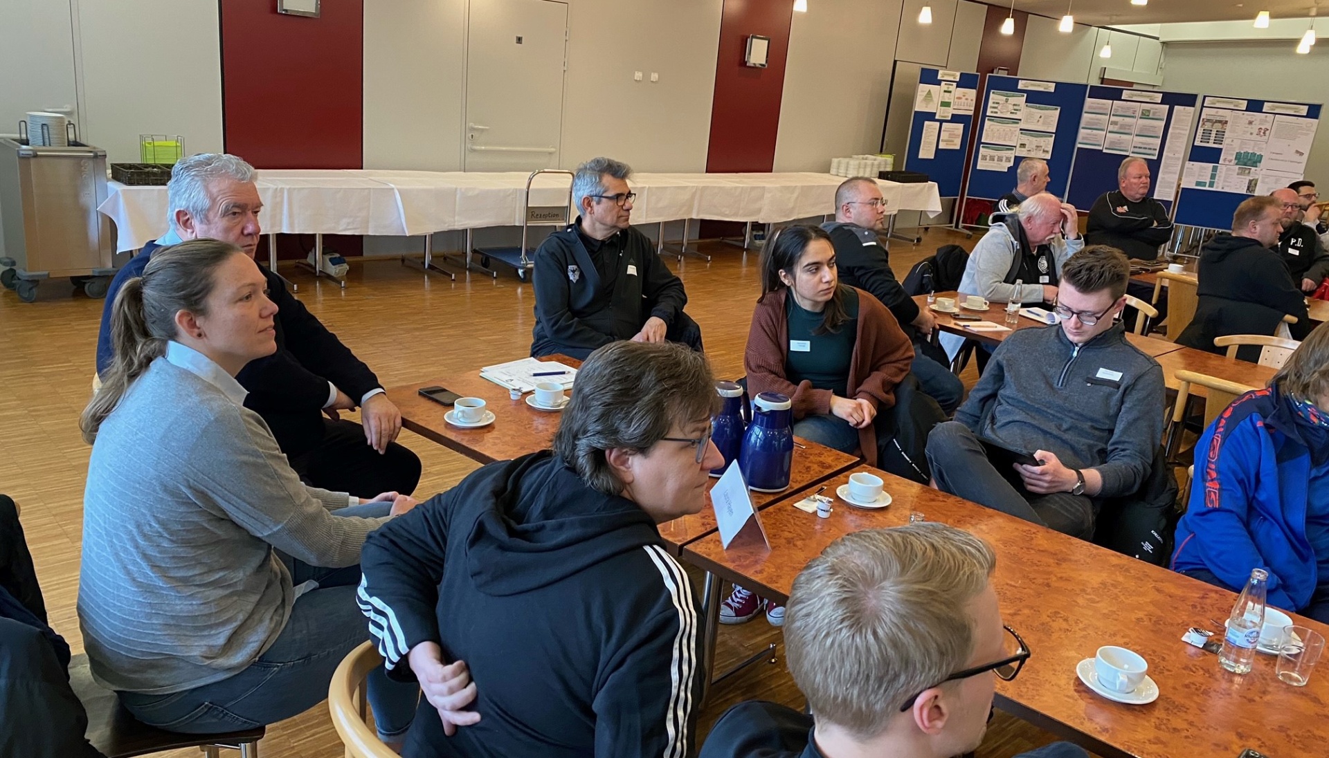 [{"clang_id":1,"value":"Versammlung von ca. 15 Personen in einem hellen Raum. Sie sitzen in einem Kreis auf Stühlen, einige mit Tassen vor sich. Im Hintergrund weitere Personen und eine Tafel."}]