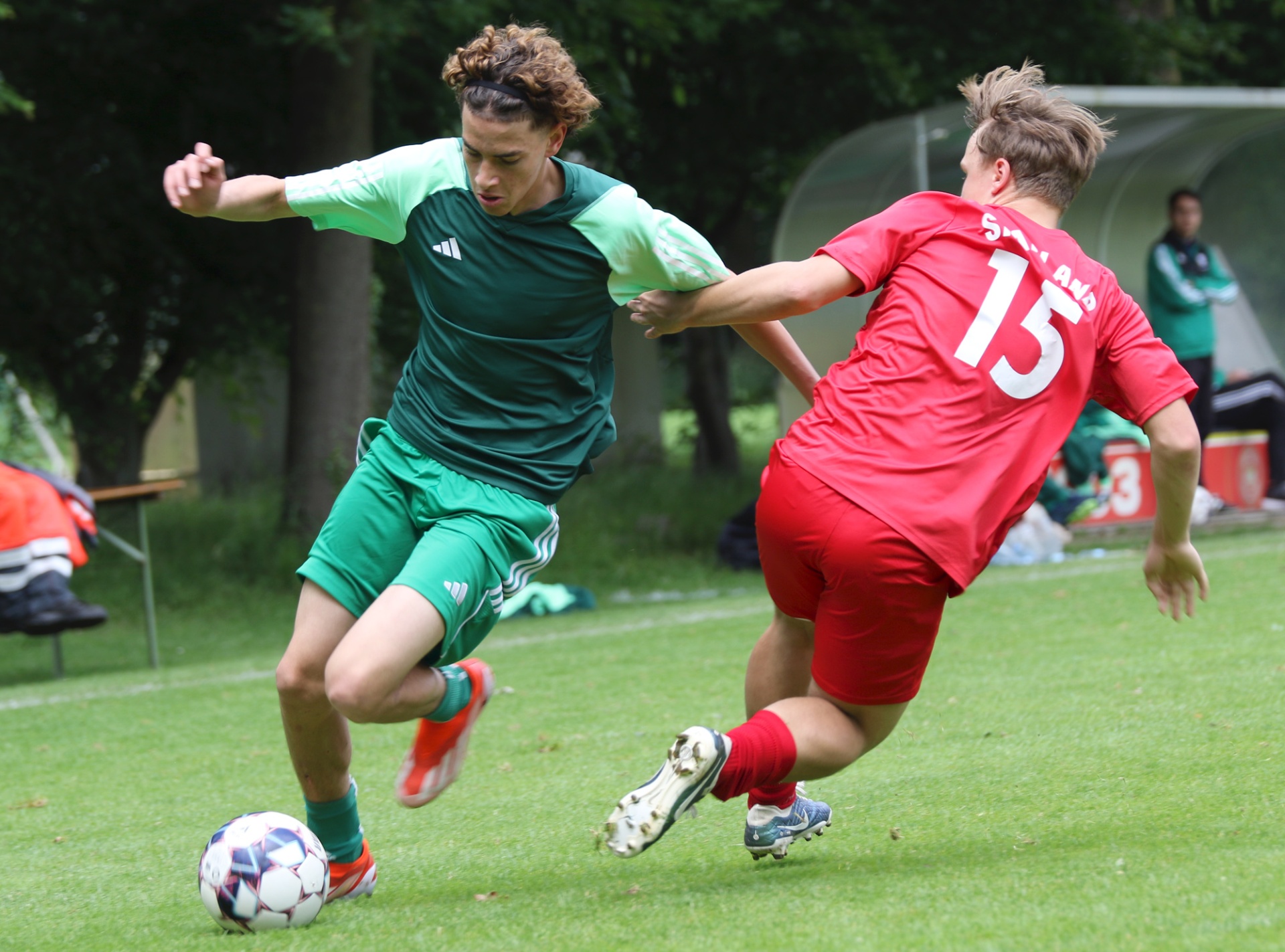 [{"clang_id":1,"value":"Zwei Fußballspieler kämpfen um den Ball auf einem grünen Rasen. Links ein Spieler in grün, rechts in rot mit der Rückennummer 15."}]