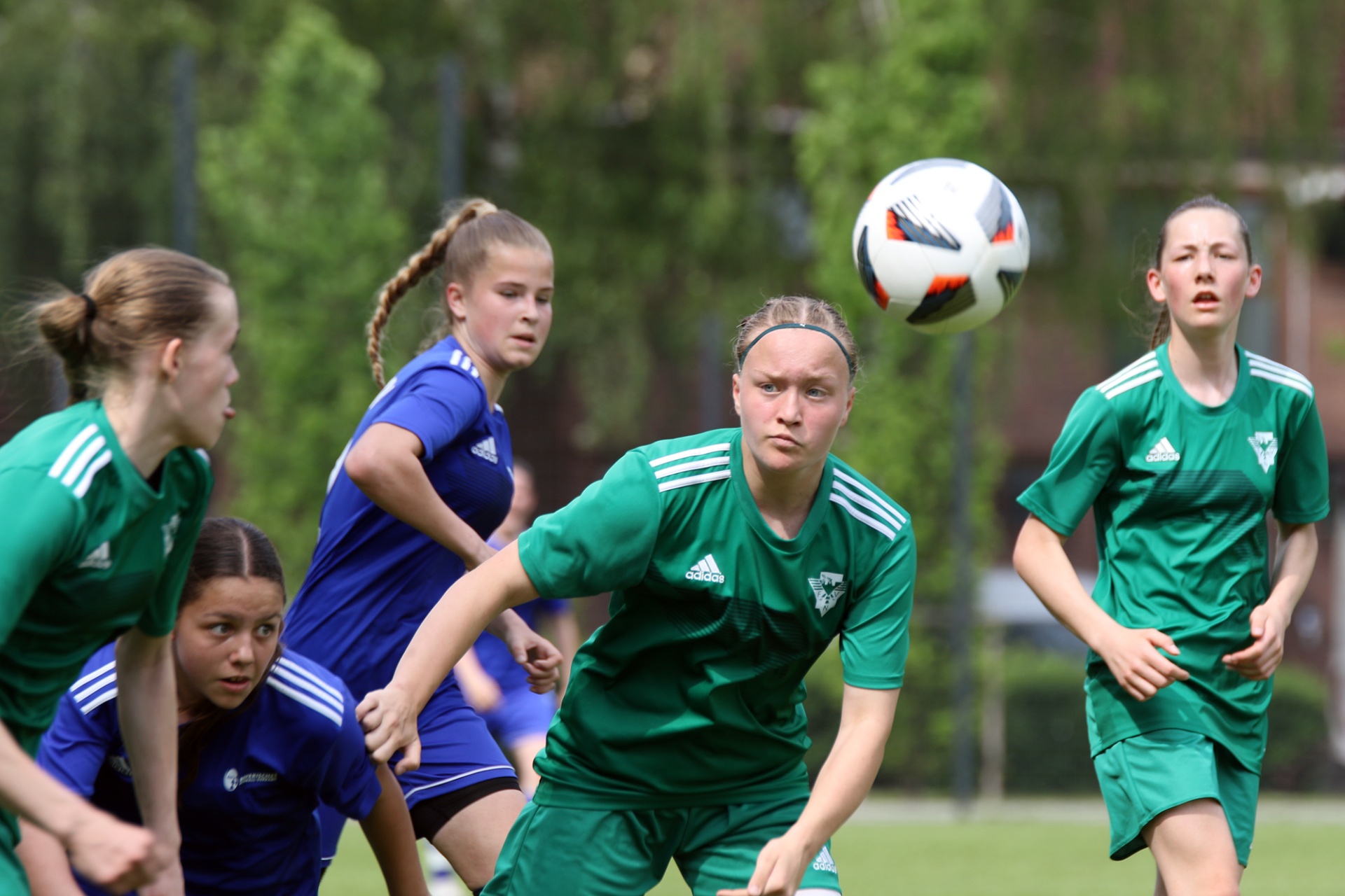 [{"clang_id":1,"value":"Fußballspiel: Mädchen in grünen und blauen Trikots kämpfen um einen Ball. Eine Spielerin köpft den Ball, andere stehen um sie herum."}]
