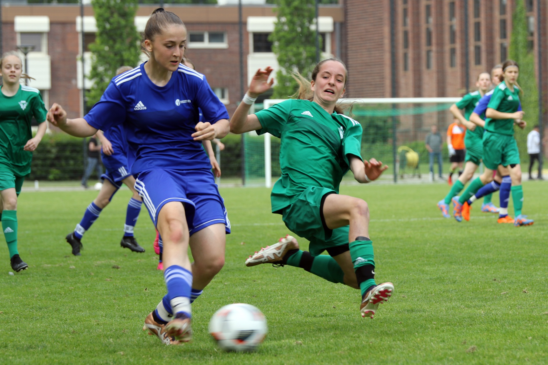 [{"clang_id":1,"value":"Fußballspiel: Zwei Spielerinnen kämpfen um den Ball. Eine in blauem, die andere in grünem Trikot. Im Hintergrund weitere Spielerinnen und ein Gebäude."}]