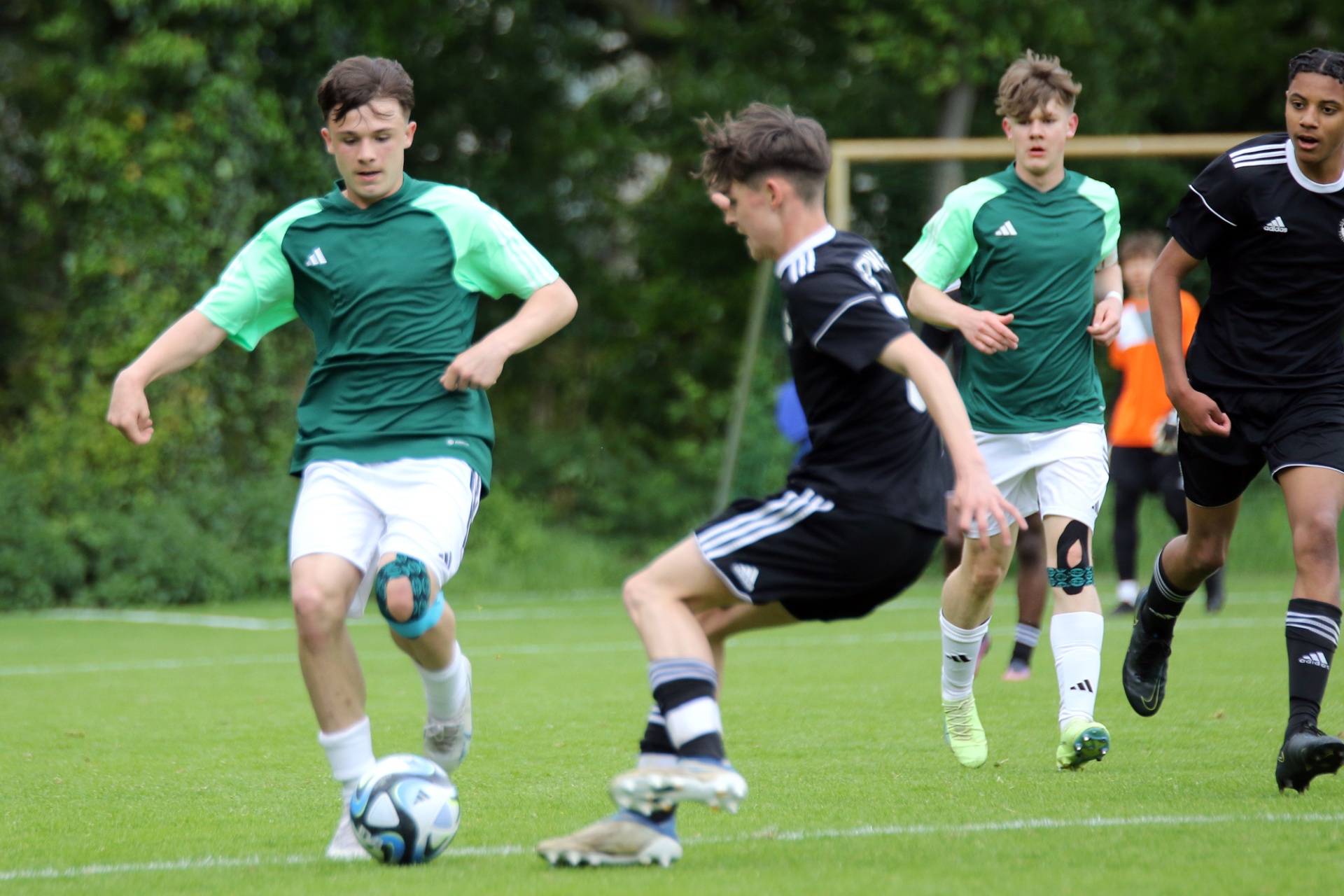[{"clang_id":1,"value":"Fußballspiel: Junge Spieler in grünen und schwarzen Trikots kämpfen um einen Ball auf einem Rasenplatz. Im Hintergrund Bäume."}]
