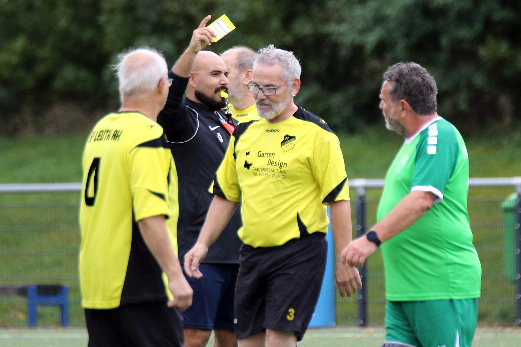 [{"clang_id":1,"value":"Fußballspiel: Schiedsrichter zeigt einem Spieler mit gelber Karte. Zwei weitere Spieler und ein Betreuer stehen in der Nähe. Grasplatz im Hintergrund."}]