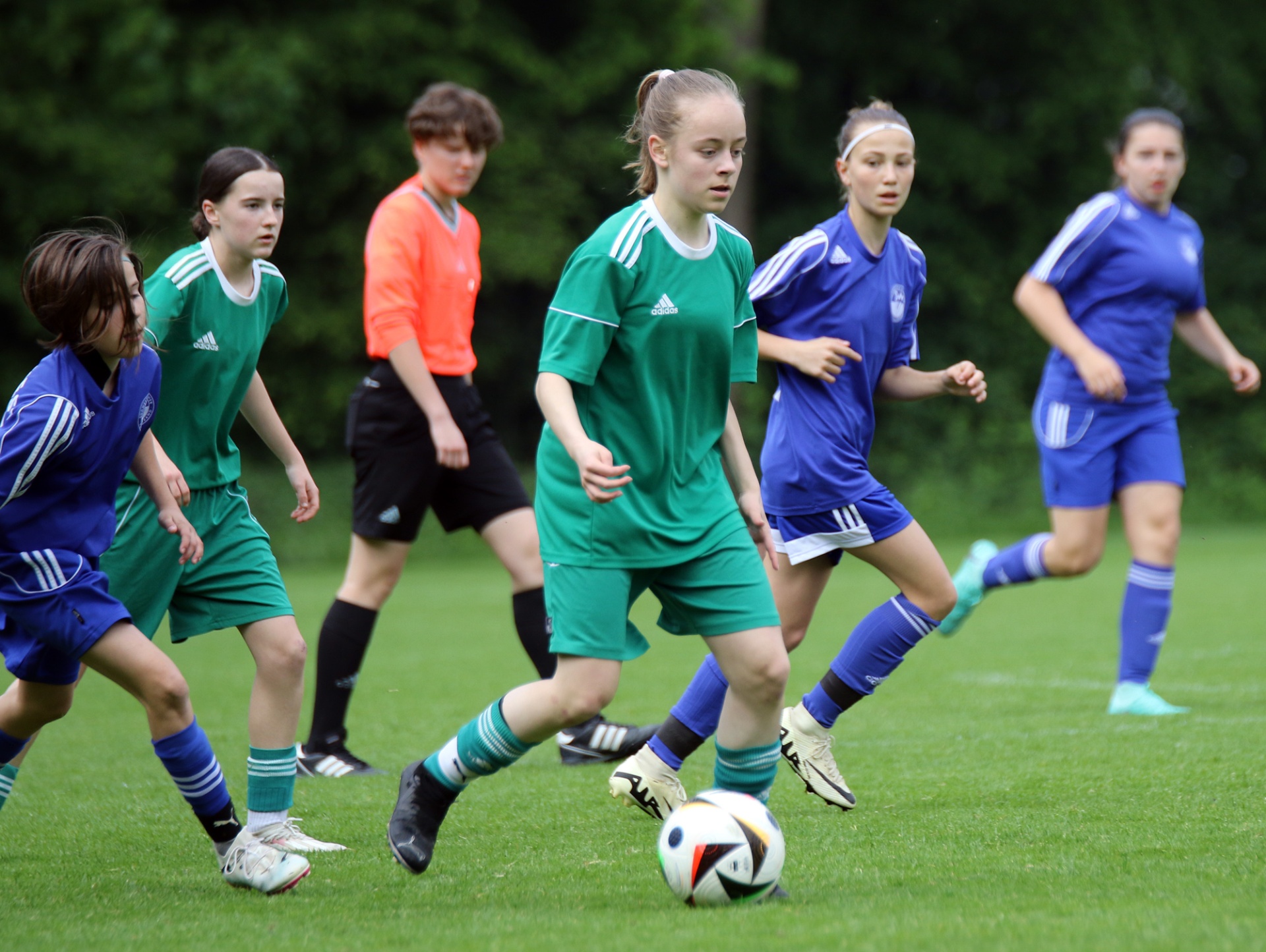 [{"clang_id":1,"value":"Fußballspiel mit jungen Spielerinnen in grünen und blauen Trikots auf Rasenfeld. Ein Schiedsrichter ist ebenfalls zu sehen."}]