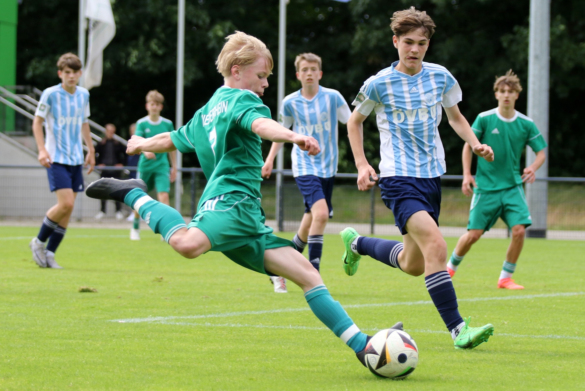 [{"clang_id":1,"value":"Junge Fussballspieler auf grünem Rasen. Ein Spieler in Grün schießt auf den Ball, ein anderer in Hellblau rennt ihm entgegen. Im Hintergrund weitere Spieler."}]
