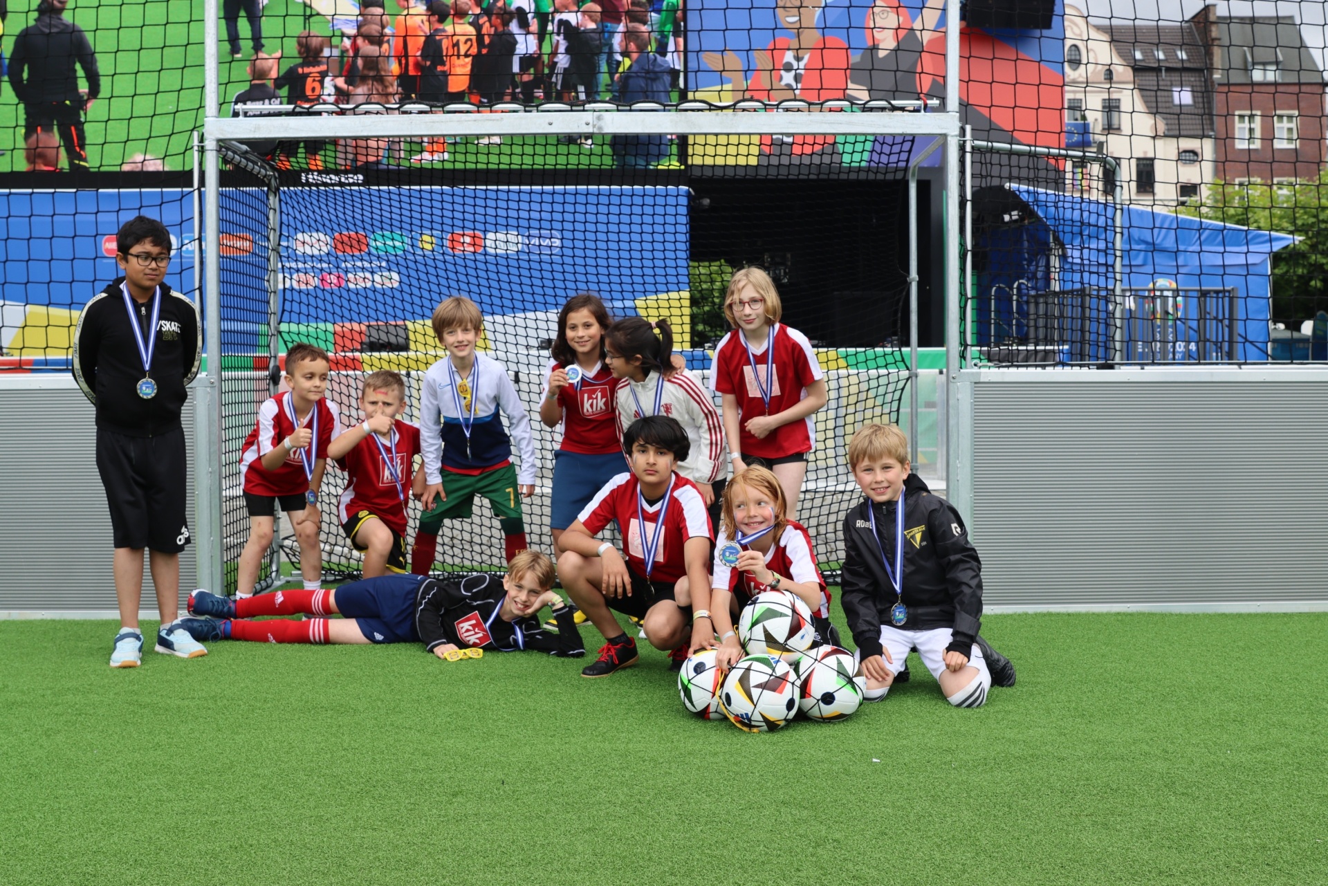 [{"clang_id":1,"value":"Fußballmannschaft mit Medaillen auf Kunstrasen. Kinder in rot-weißen Trikots sitzen oder knien vor einem Fußballtor."}]
