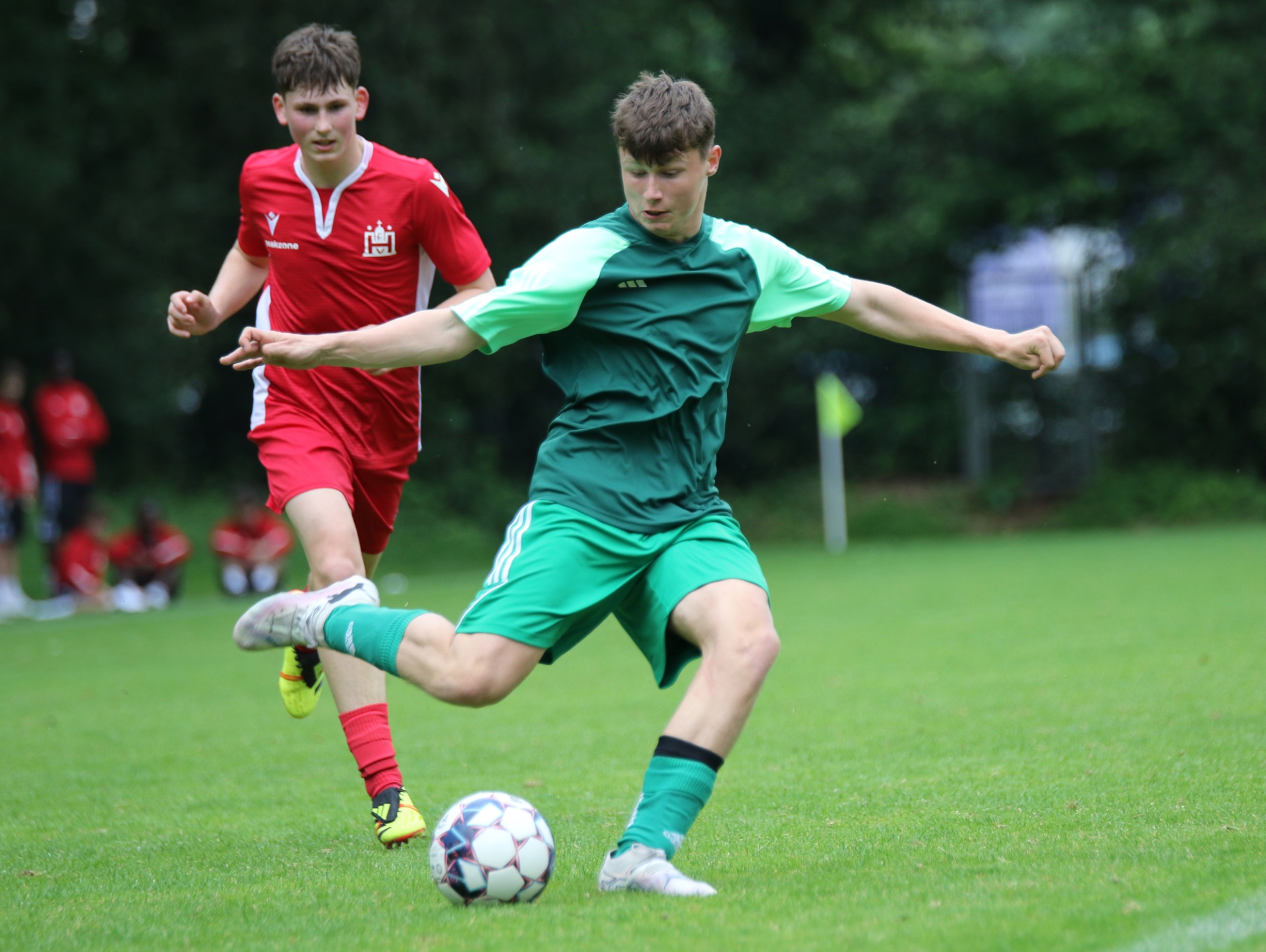 [{"clang_id":1,"value":"Zwei Fußballspieler auf grünem Rasen. Vorne ein Spieler in grüner Sportbekleidung beim Schuss, dahinter ein Spieler in rotem Trikot."}]