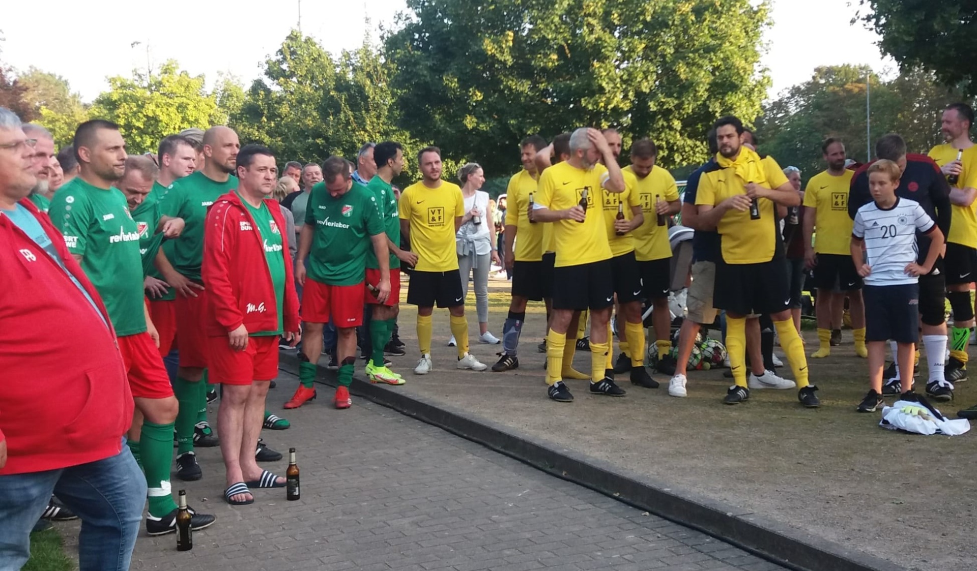[{"clang_id":1,"value":"Fußballspieler in zwei Teams stehen sich nach einem Spiel gegenüber und applaudieren. Einige Personen tragen rote Jacken, andere gelbe oder grüne Trikots."}]