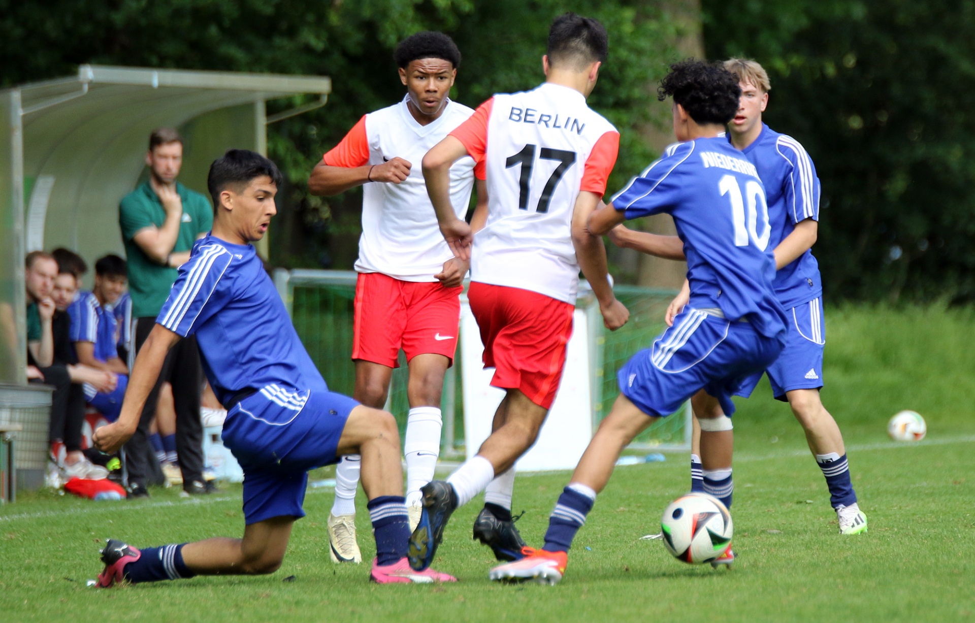 [{"clang_id":1,"value":"Jugendfußballspiel auf Rasenplatz. Vier Spieler in farbigen Trikots kämpfen um den Ball. Im Hintergrund Zuschauer und ein Pavillon."}]
