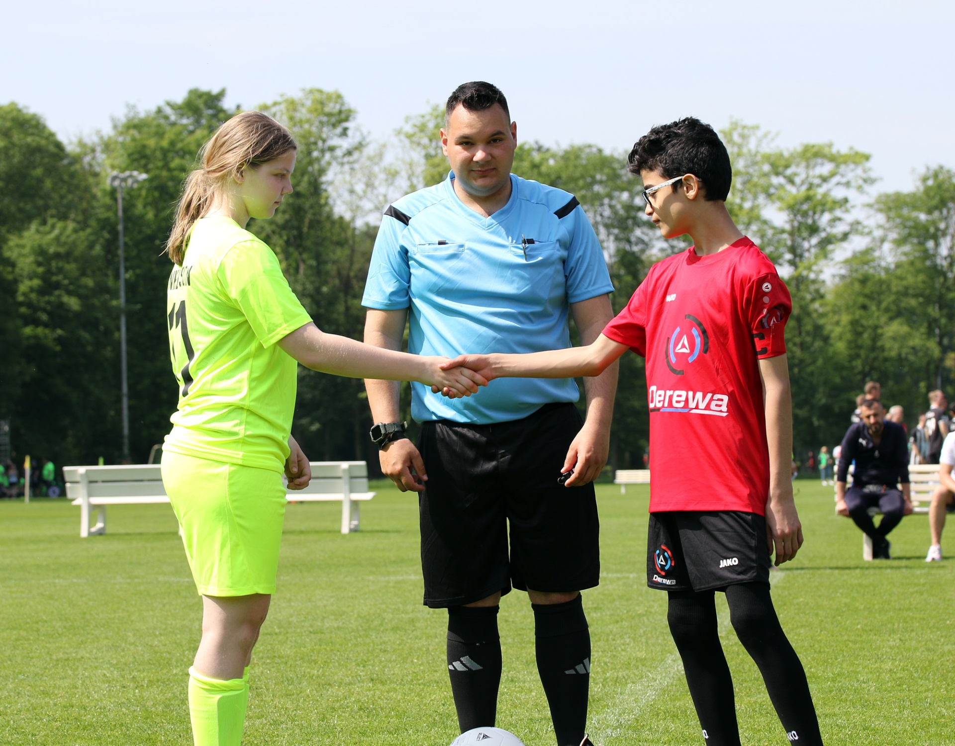 [{"clang_id":1,"value":"Fußball: Schiedsrichter schüttelt zwei Spielerinnen (gelb/rot) vor dem Spiel die Hand. Im Hintergrund ein Fußballfeld und Zuschauer."}]