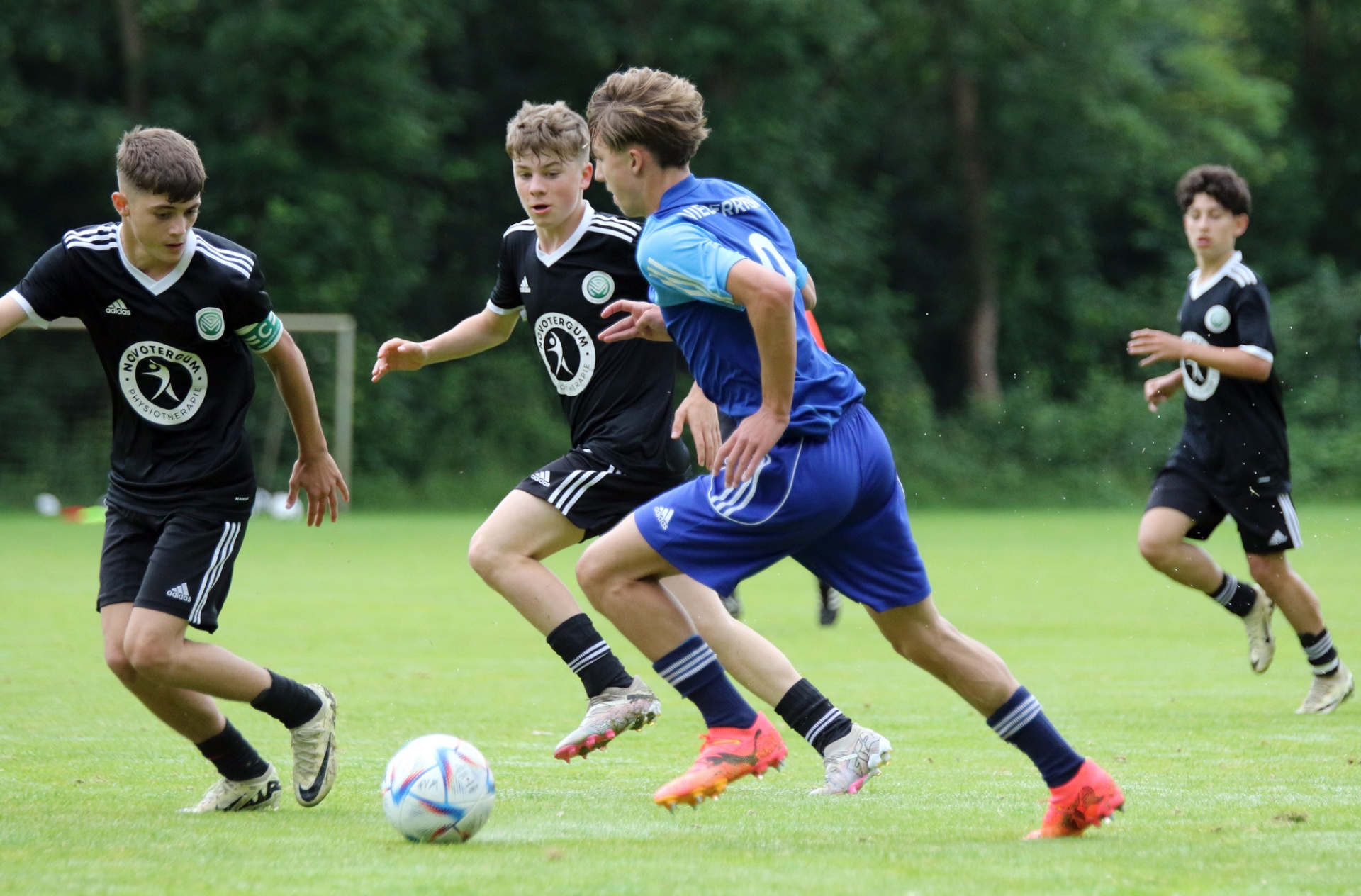 [{"clang_id":1,"value":"Fußballspiel: Vier jugendliche Spieler auf grünem Rasen. Zwei in schwarzen Trikots, einer in blauem Trikot kämpfen um den Ball. Im Hintergrund ein weiterer Spieler."}]