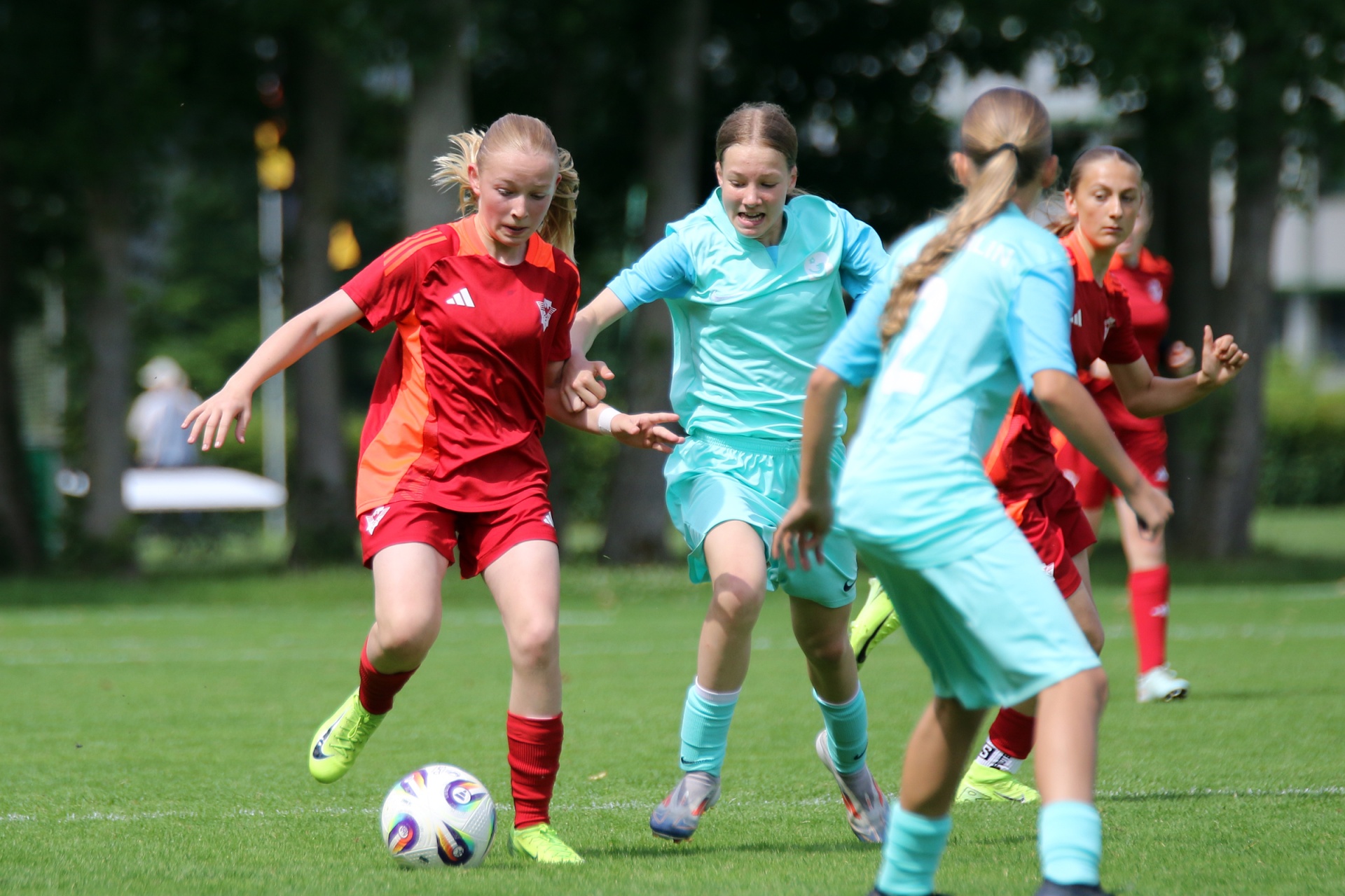 [{"clang_id":1,"value":"Fußballspiel: Zwei Mädchen in Rot und Türkis kämpfen um den Ball auf einem grünen Rasen. Weitere Spieler im Hintergrund."}]