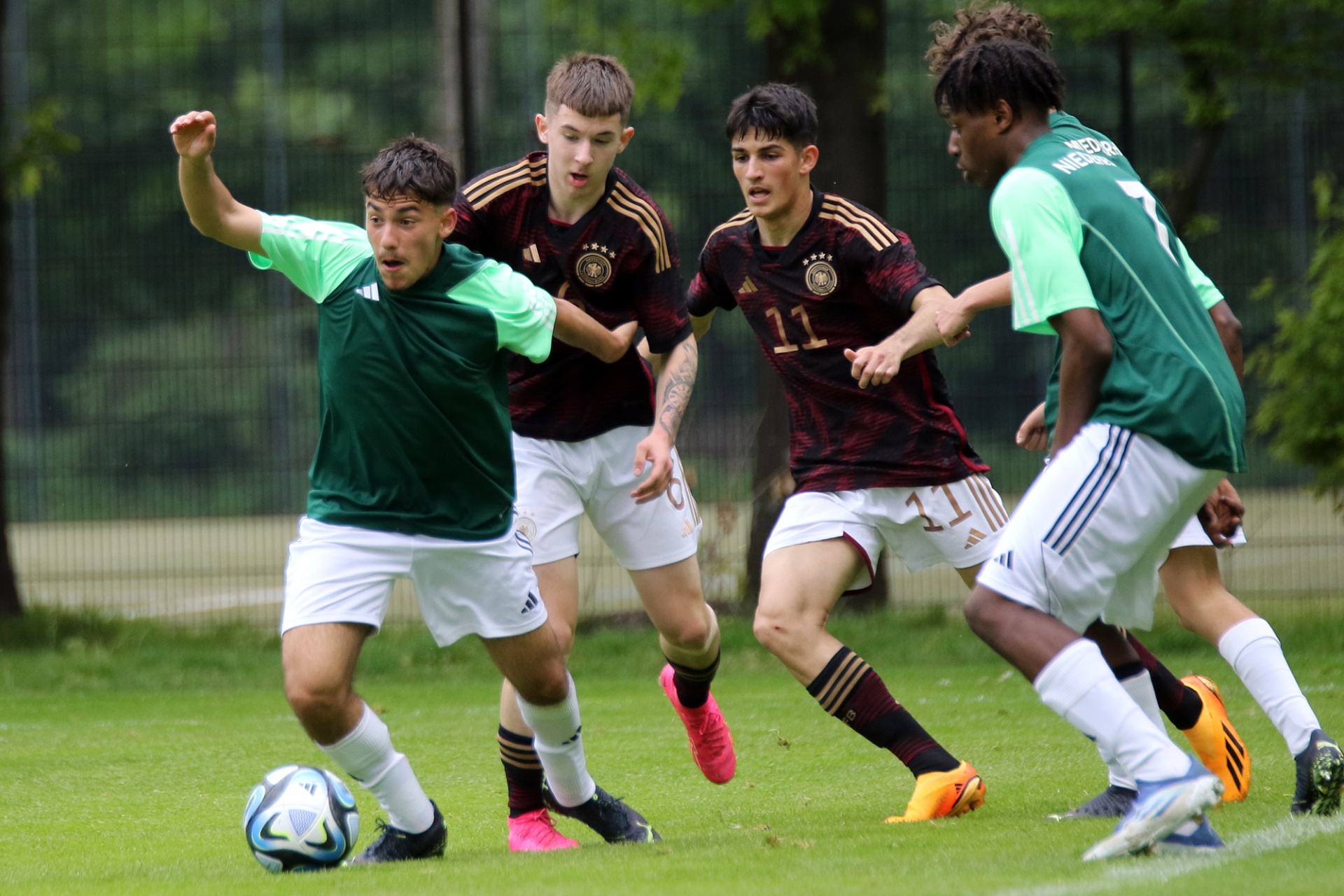 [{"clang_id":1,"value":"Fußballspiel: Zwei Spieler in dunkelroten Trikots mit Nummer 11 und zwei Spieler in grünen Trikots kämpfen um einen Ball auf einem Rasenplatz."}]